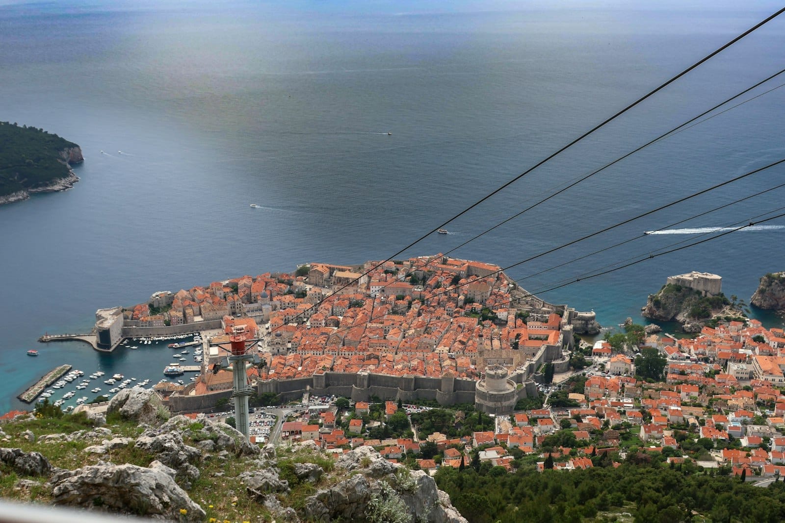 Vista panorámica desde el monte Srđ con el casco antiguo de Dubrovnik, el mar Adriático, la isla de Lokrum y los cables del teleférico descendiendo hacia la ciudad.