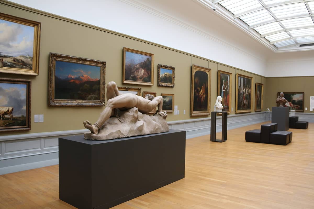 Sculptures and framed paintings displayed in a spacious, well-lit gallery at the Museum of Fine Arts Ghent, with wood flooring and modern seating.