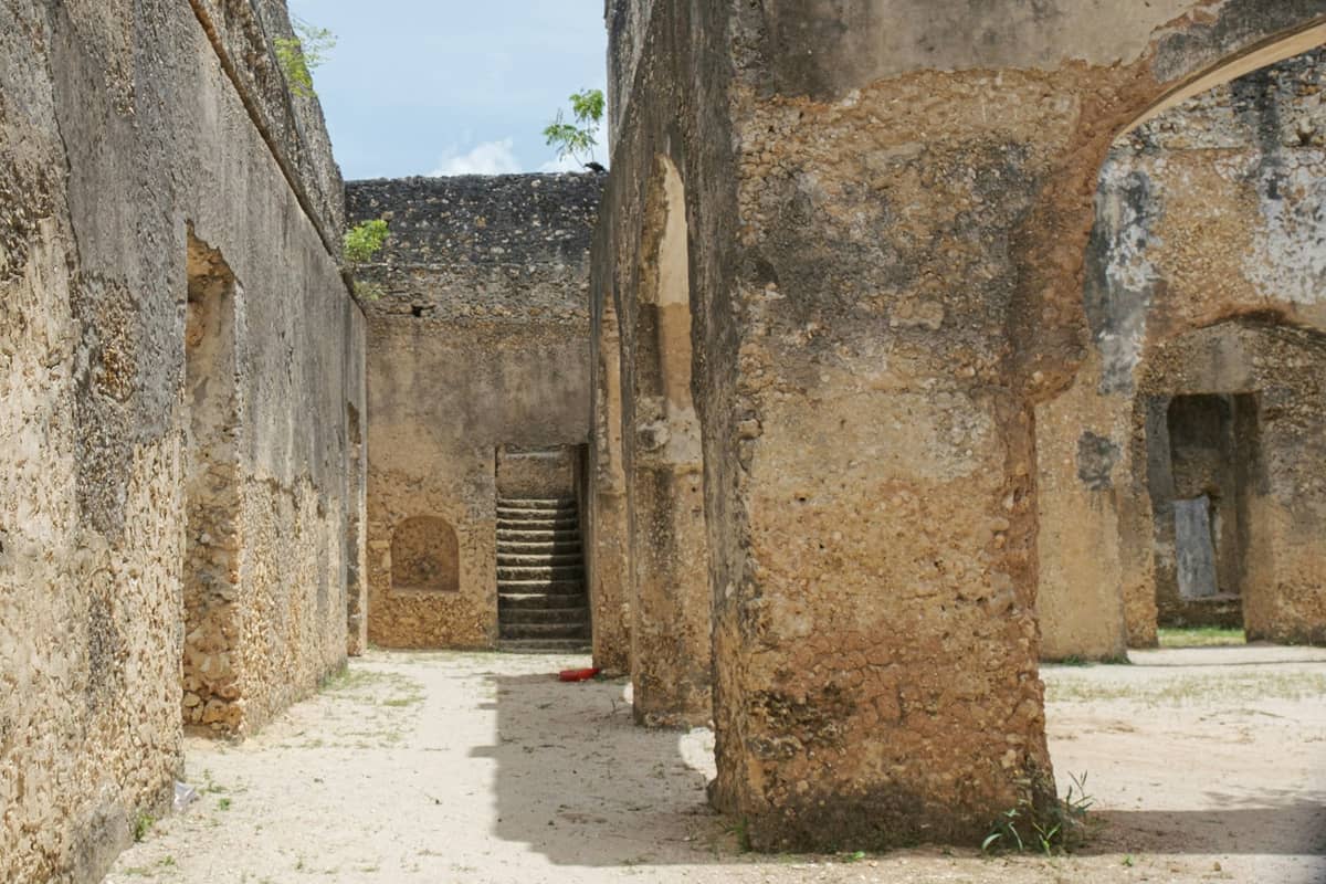 Wnętrze ruin Pałacu Mtoni na Zanzibarze – stare kamienne mury, łuki i schody z wypiaszczałą, zniszczoną posadzką.