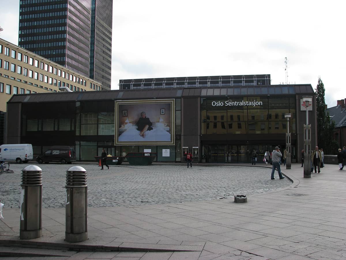 วิวภายนอกของ Oslo Sentralstasjon พร้อมผู้คนที่เดินอยู่ด้านหน้า อาคารสมัยใหม่เป็นฉากหลัง และป้ายที่เขียนว่า 'Oslo Sentralstasjon'