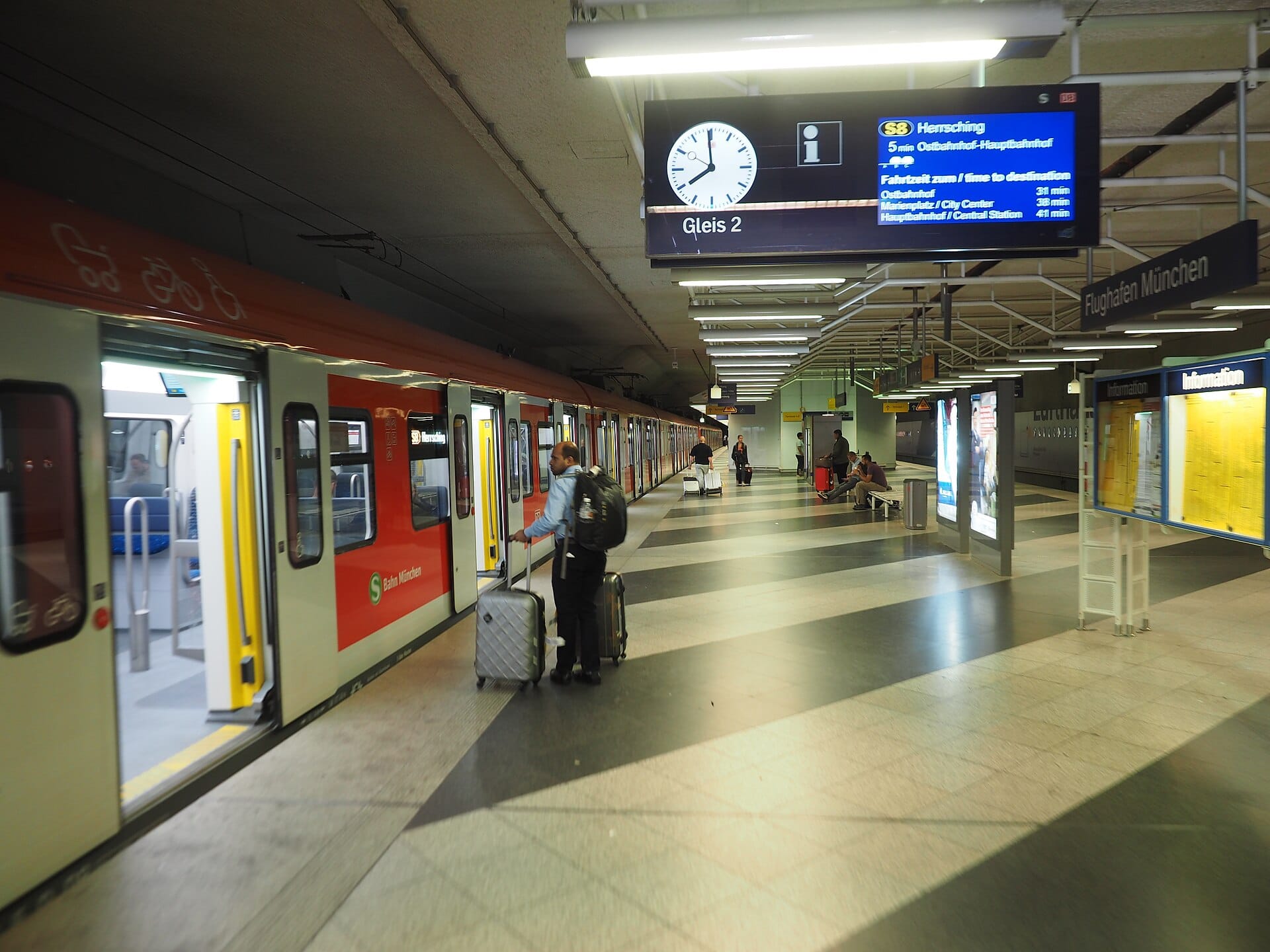 ผู้โดยสารพร้อมสัมภาระขึ้นรถไฟ S-Bahn ที่สถานีใต้ดินของ Munich Airport พร้อมป้ายบอกทางสาย S1 และ S8 สู่ใจกลางเมือง