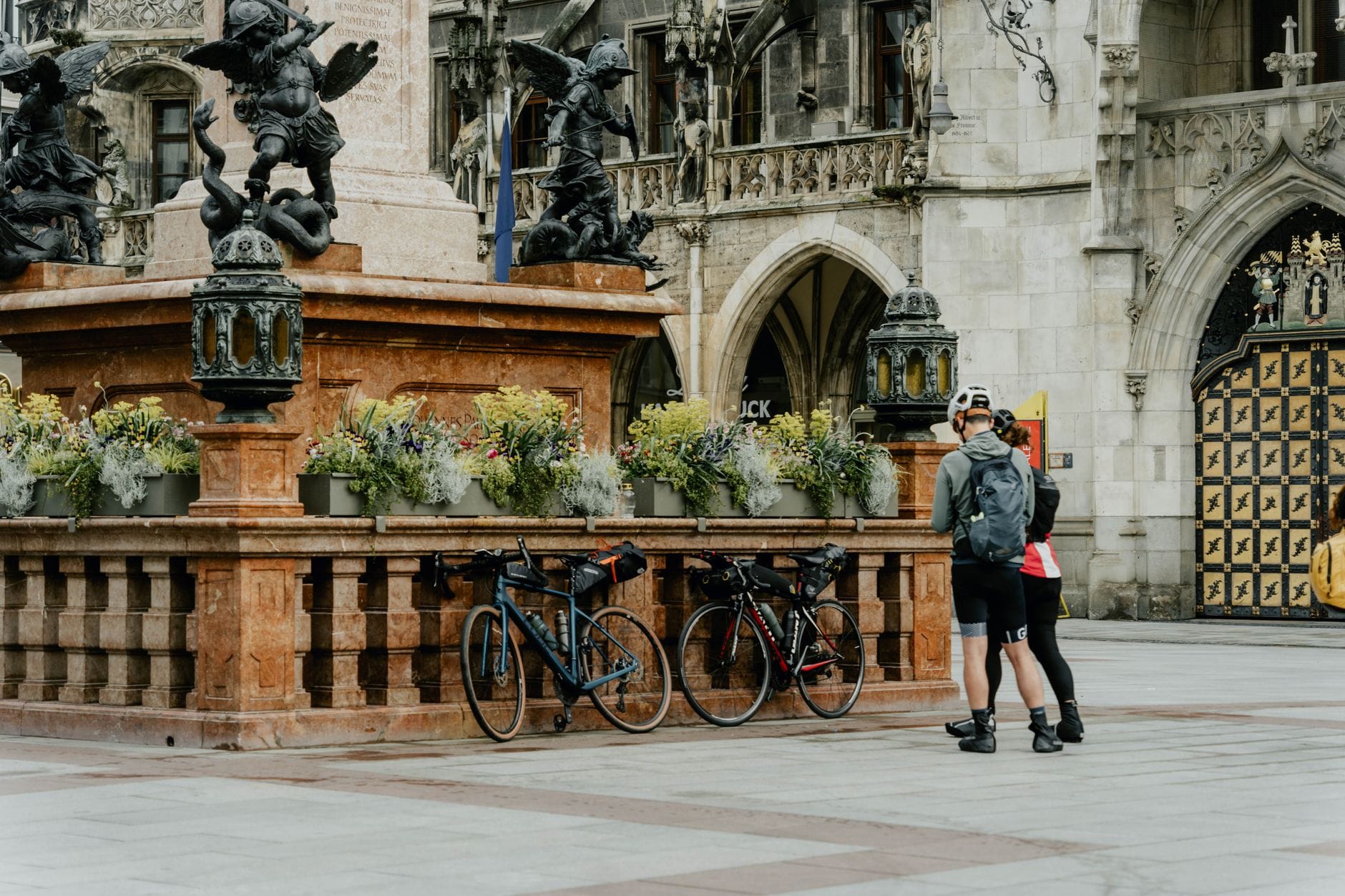 นักปั่นจักรยานพักผ่อนพร้อมจักรยานที่น้ำพุประวัติศาสตร์ใจกลาง Munich โดยมีสถาปัตยกรรมประดับประดาเป็นฉากหลัง
