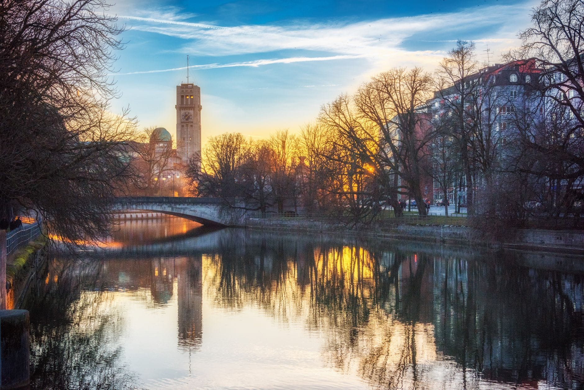 วิวสวยงามของแม่น้ำ Isar ในเมือง München ยามพระอาทิตย์ตก พร้อมอาคารประวัติศาสตร์และหอคอย Deutsches Museum ที่สะท้อนอยู่บนผิวน้ำ
