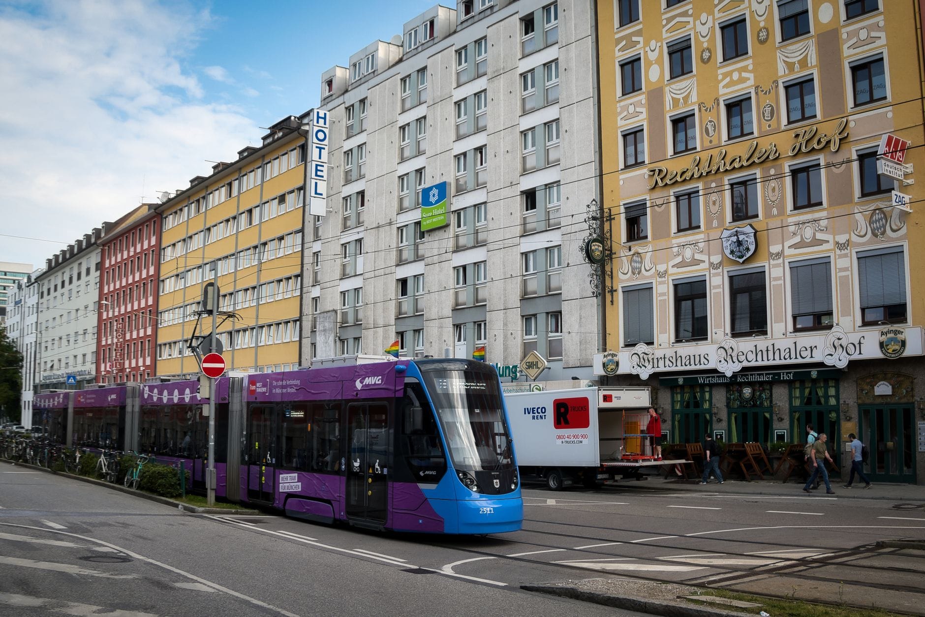 วิวถนนของโรงแรมและที่พักราคาประหยัดใกล้สถานีกลาง Munich พร้อมรถรางสีม่วงและผู้คนนอกร้านอาหาร