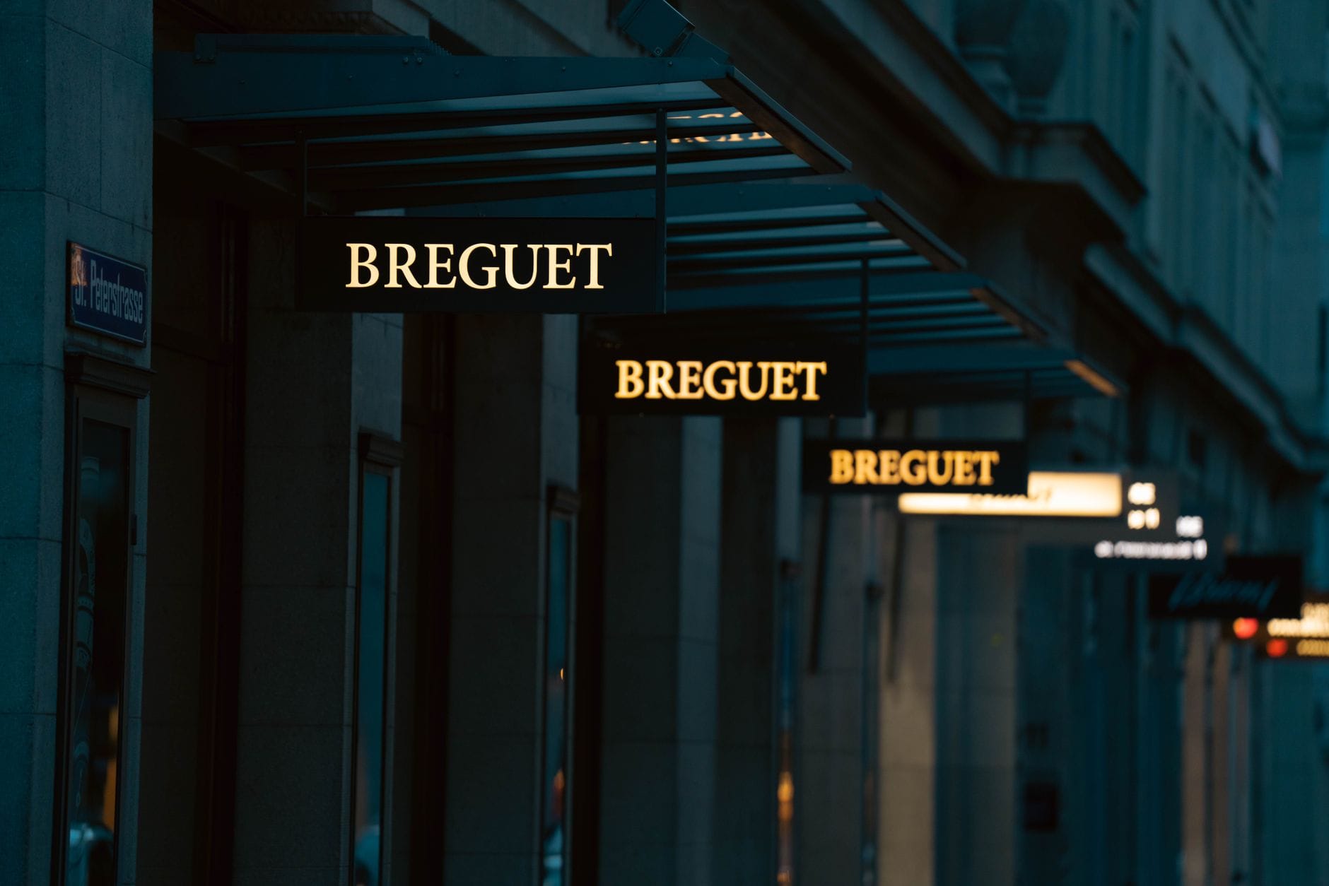 ป้ายร้านบูติกนาฬิกาหรู Breguet ที่สว่างไสวบนถนนช้อปปิ้งชั้นสูงในมิวนิกยามพลบค่ำ