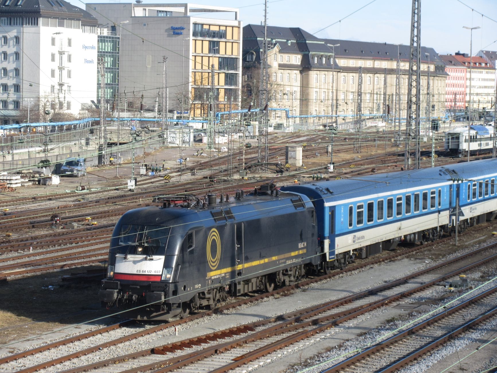 รถไฟสายระหว่างประเทศมิวนิก-ปราก ตู้โดยสารสีน้ำเงินของ Czech Railways หัวรถจักรสีดำ จอดที่สถานี Munich Hauptbahnhof เห็นรางรถไฟและตึกในเมืองเบื้องหลัง