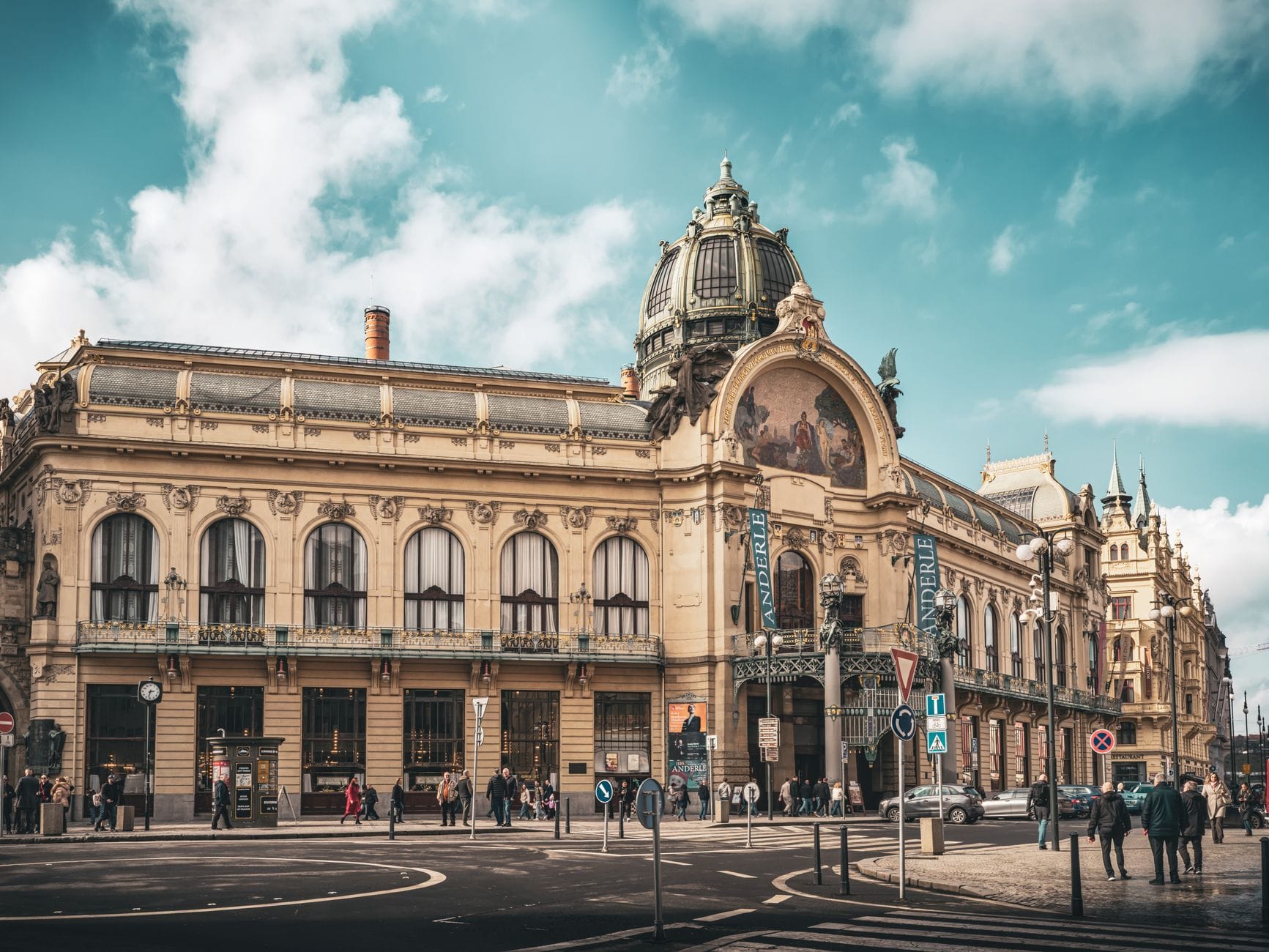 Vista ampia della Casa Municipale di Praga con la sua sontuosa facciata Art Nouveau, l'ingresso principale, la cupola e la gente fuori in una giornata luminosa.
