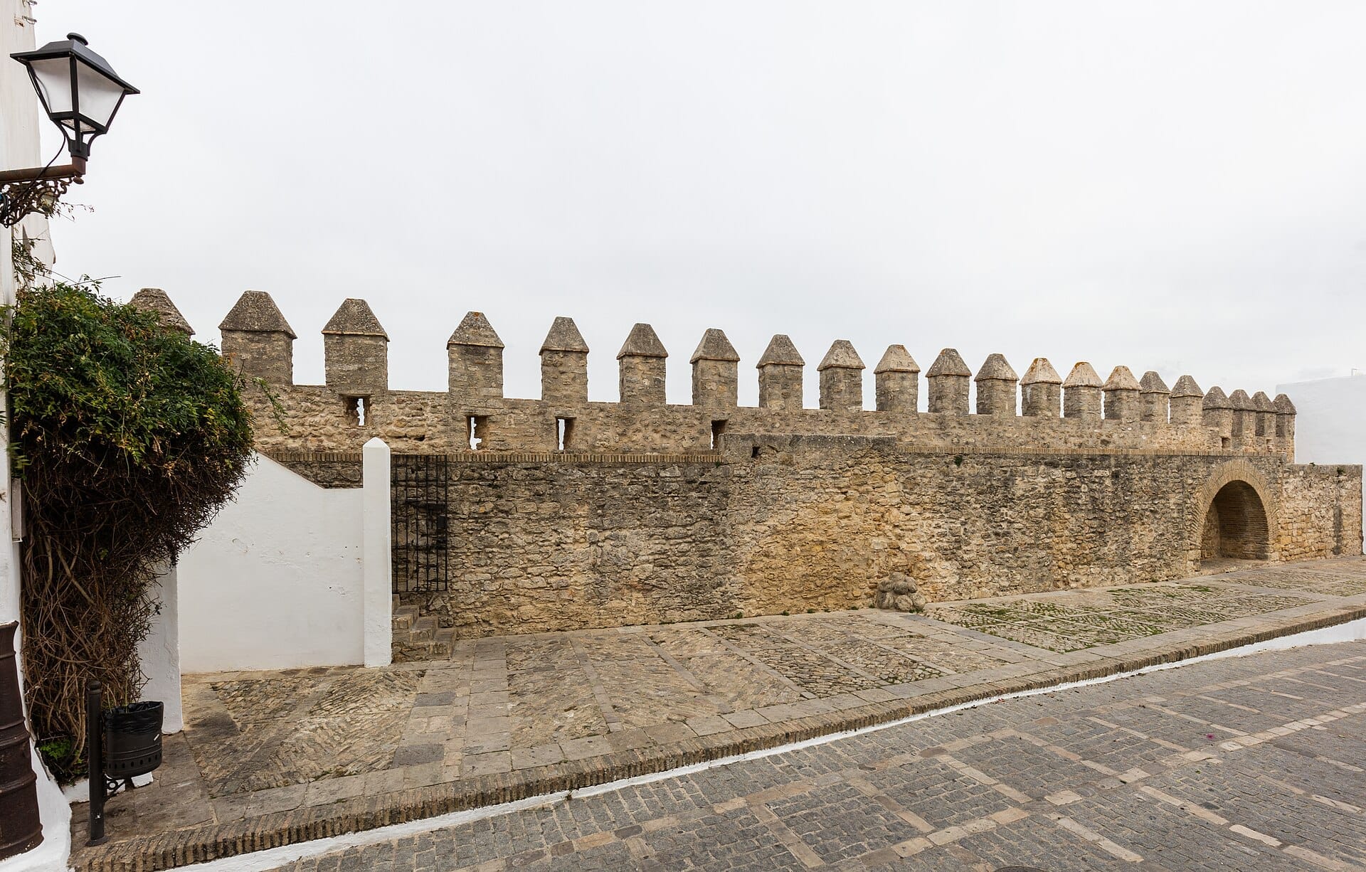 Stone battlements of the Murallas de Cádiz with a historic arched entrance, cobbled walkway, and soft daylight under an overcast sky.