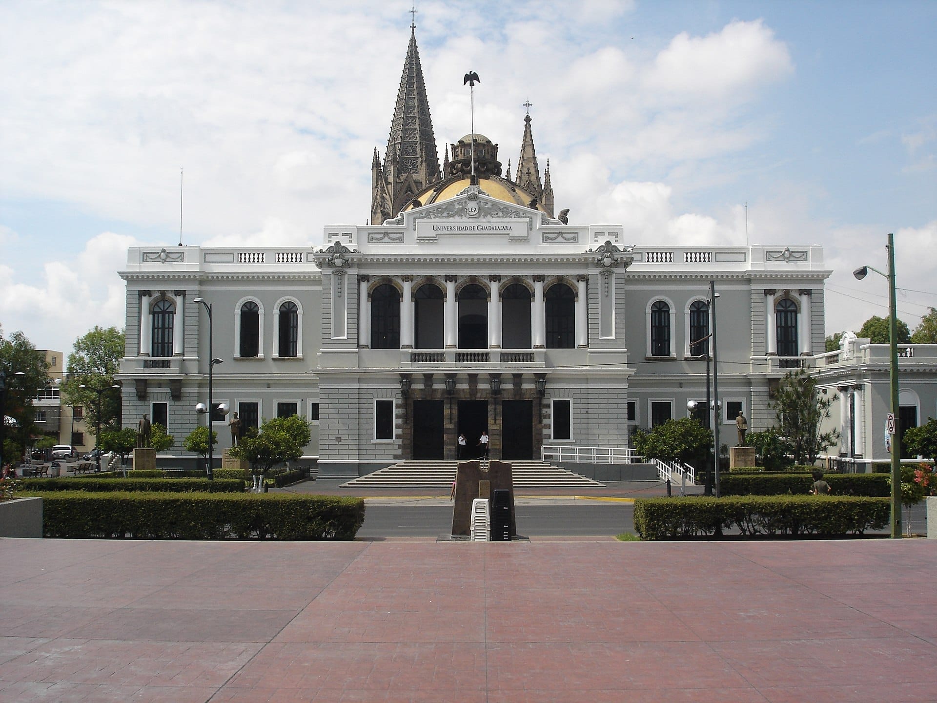 Ornata facciata neoclassica bianca del MUSA, Museo de las Artes de la Universidad de Guadalajara, con guglie e cupola sotto un cielo parzialmente nuvoloso.