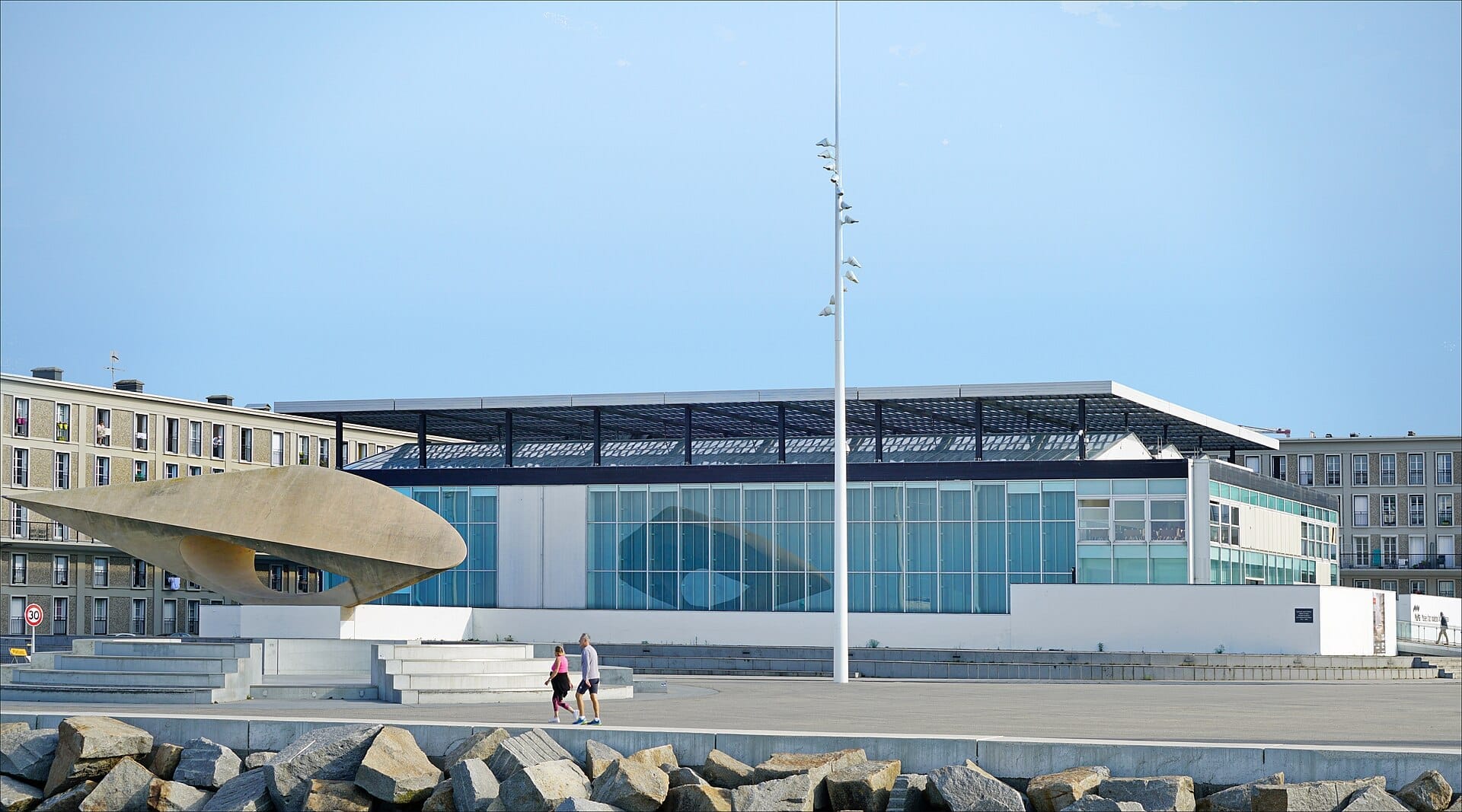 Le Havre'daki Musée d'Art Moderne André Malraux'nun cam cephesi, modern heykeli ve açık bir gökyüzü altında geniş gezinti yoluyla dış görünümü.