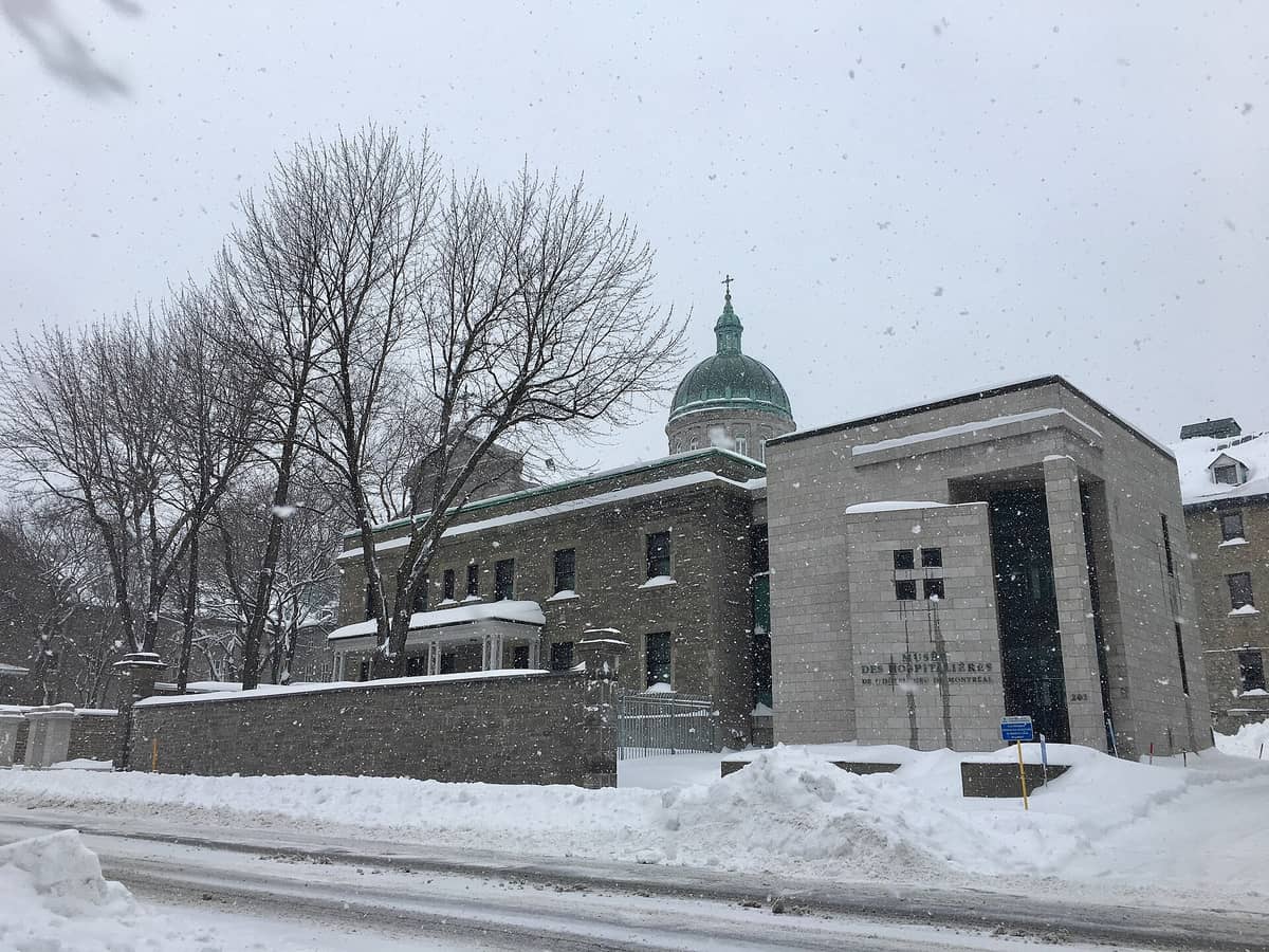 Verschneite Winterstraße mit Blick auf das Musée des Hospitalières de l'Hôtel-Dieu de Montréal mit seiner markanten Kuppel und dem Museumseingang.