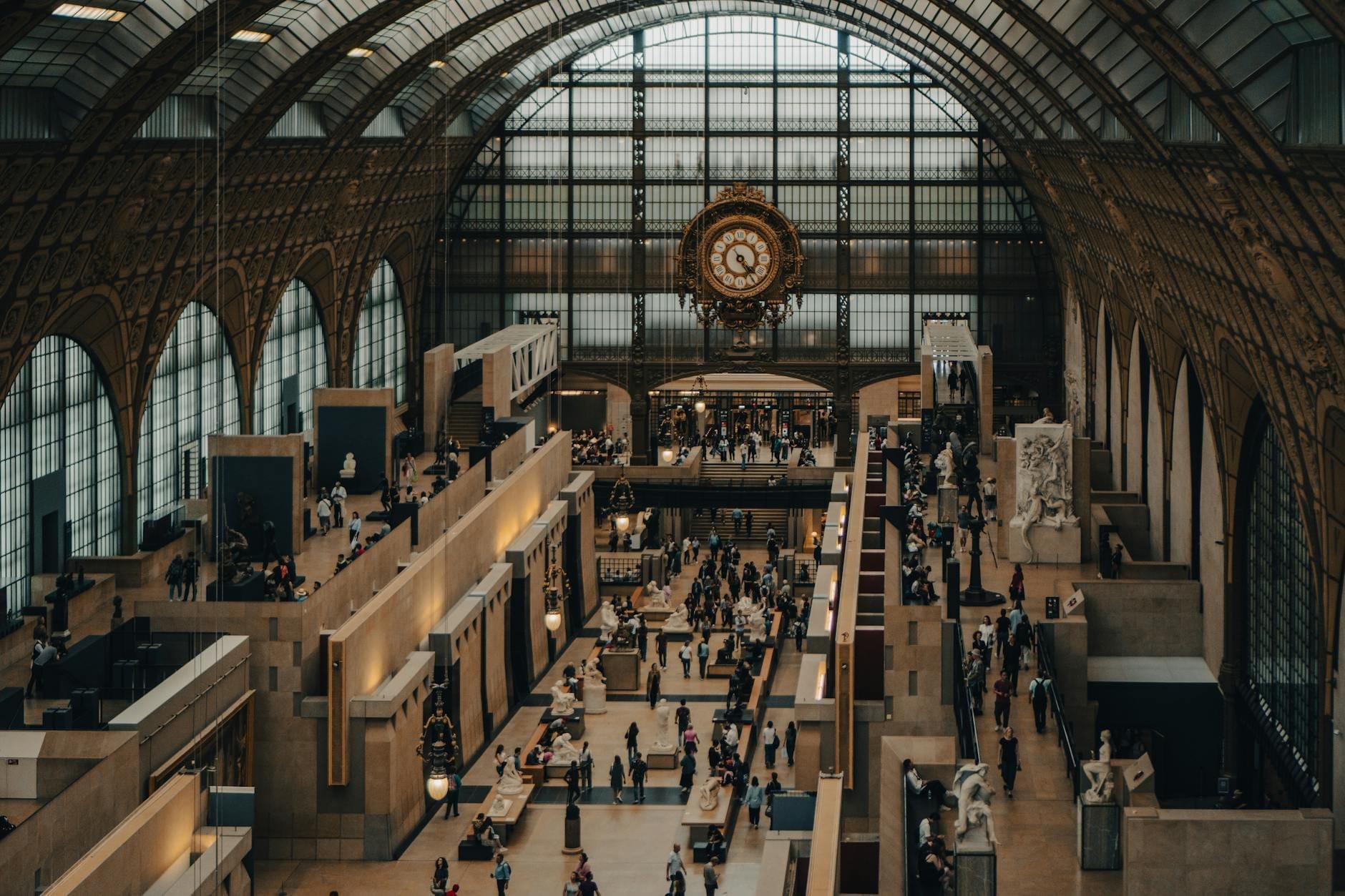 Vista panoramica dell'interno del Musée d'Orsay con la sua grande volta in ferro e vetro, il celebre orologio centrale, i visitatori in movimento e le sculture esposte.