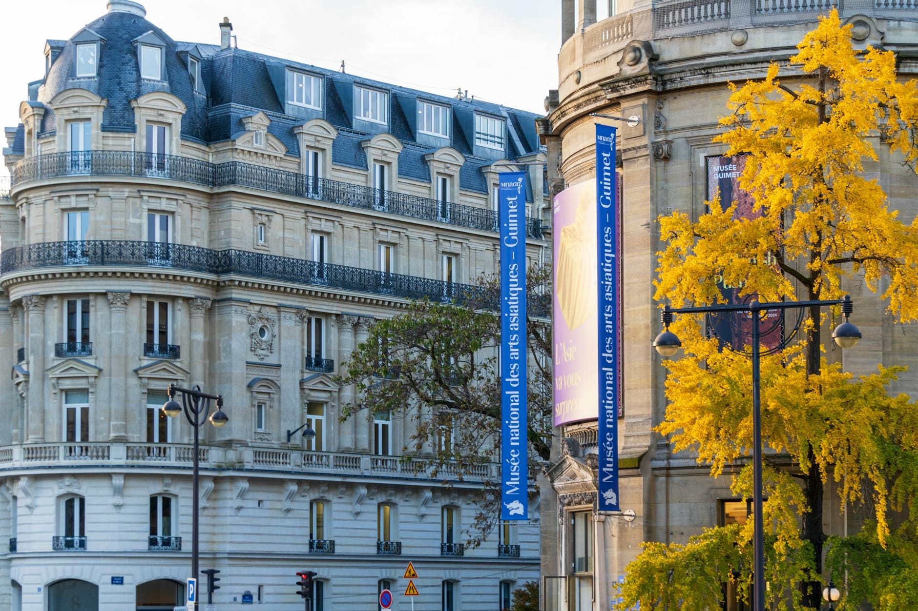 Elegante edificio neoclassico con striscioni blu con la scritta 'Musée national des arts asiatiques – Guimet', circondato da alberi e architettura urbana in una giornata di sole.