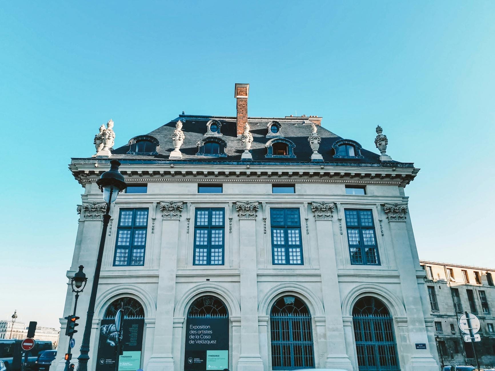 Facciata di un elegante palazzo parigino con finestre ad arco, statue ornamentali sul tetto e cielo azzurro sullo sfondo.