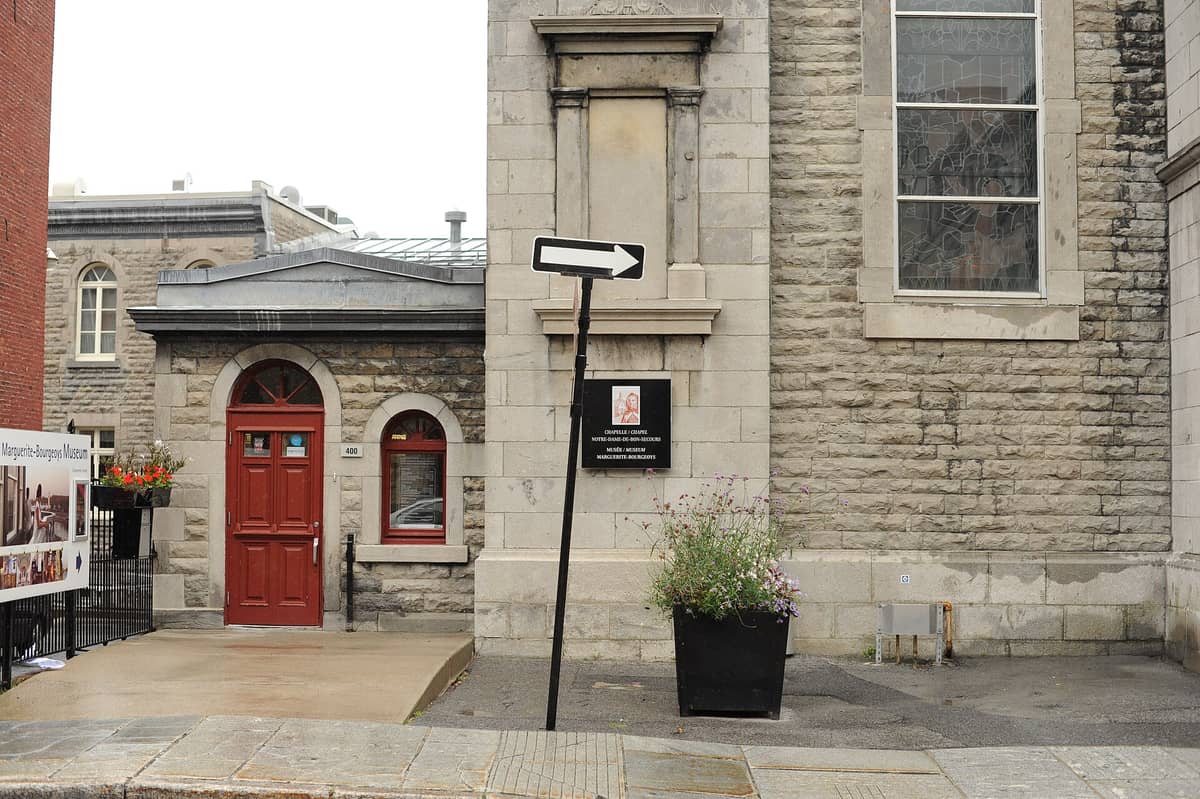 Eingangsbereich des Musée Marguerite-Bourgeoys im Alten Montreal mit roter Tür, Steinmauern und gut sichtbarem Museumsschild.