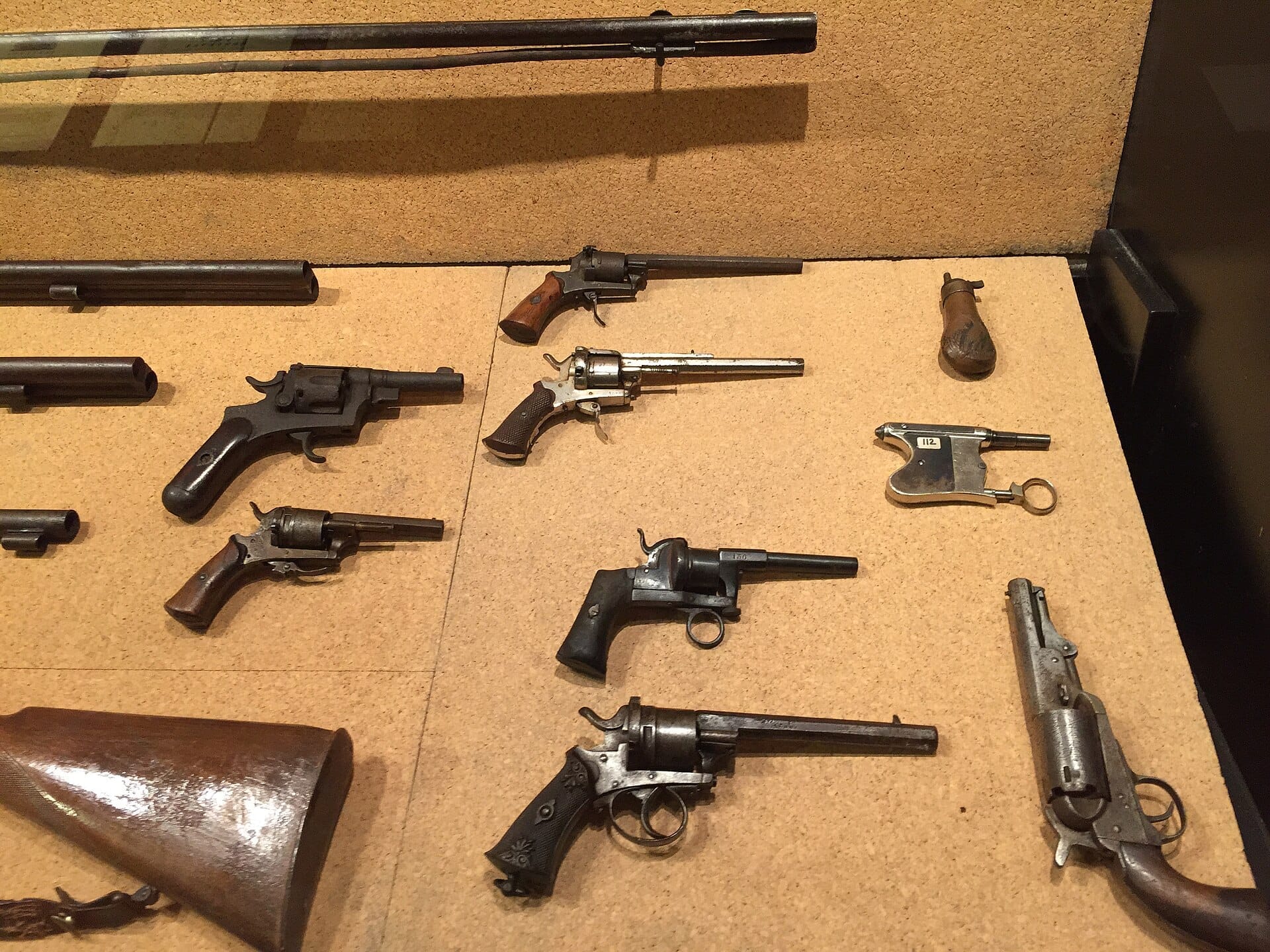 Vitrine im Inneren des Museo del Banditismo di Aggius mit einer Reihe antiker Pistolen und Schusswaffen auf einem Korkhintergrund.