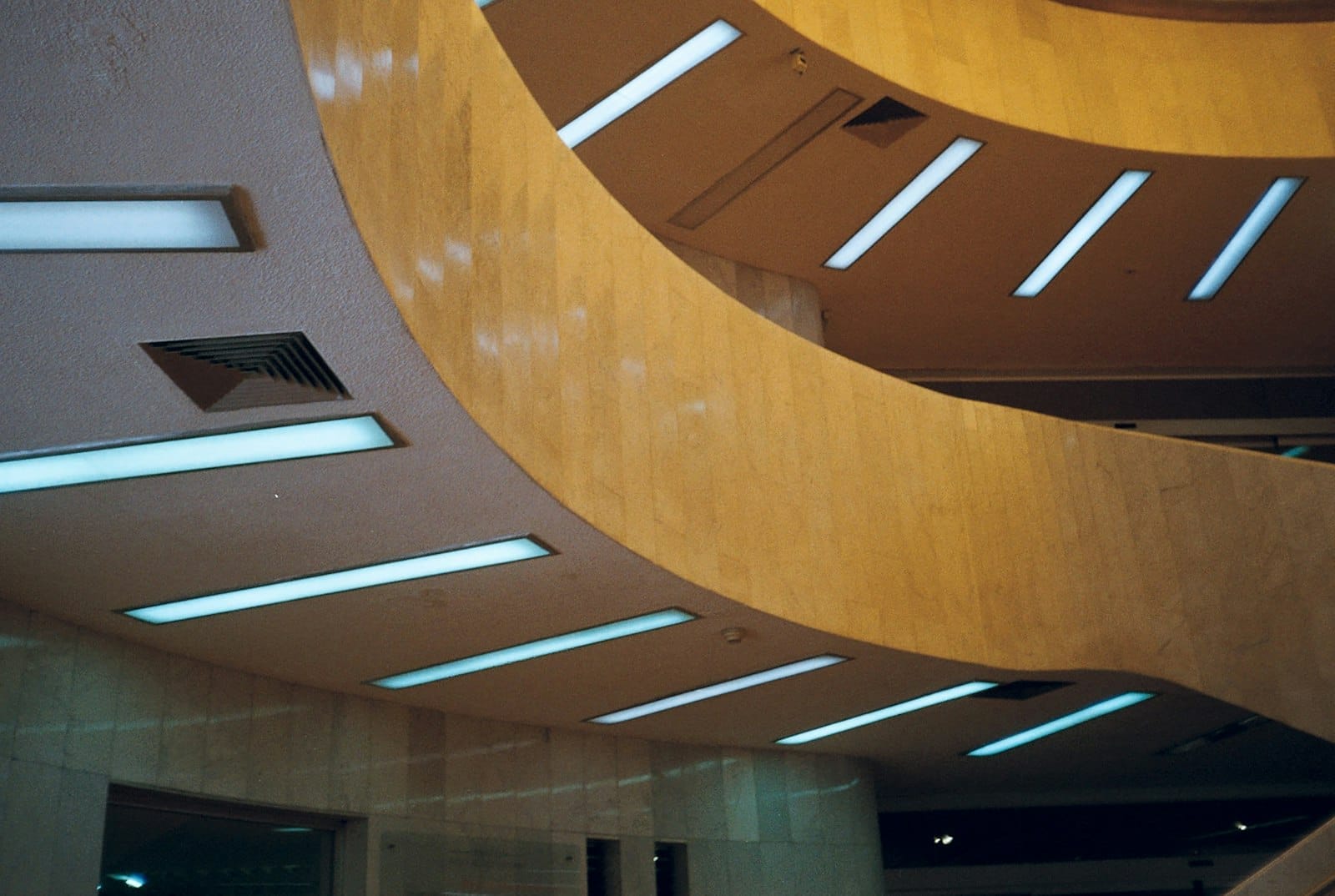Interno architettonico curvilineo del Museo de Arte Moderno con pareti in pietra beige e file di luci moderne blu sul soffitto.