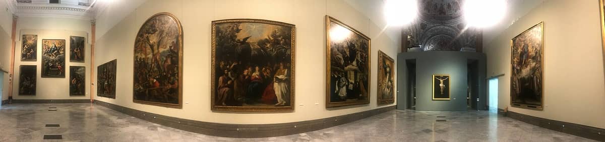 มุมมองกว้างของหอศิลป์ Museo de Bellas Artes de Sevilla ที่จัดแสดงภาพวาดขนาดใหญ่สมัย Golden Age บนผนังสีครีมและพื้นหินอ่อนภายใต้แสงไฟอ่อนนุ่ม