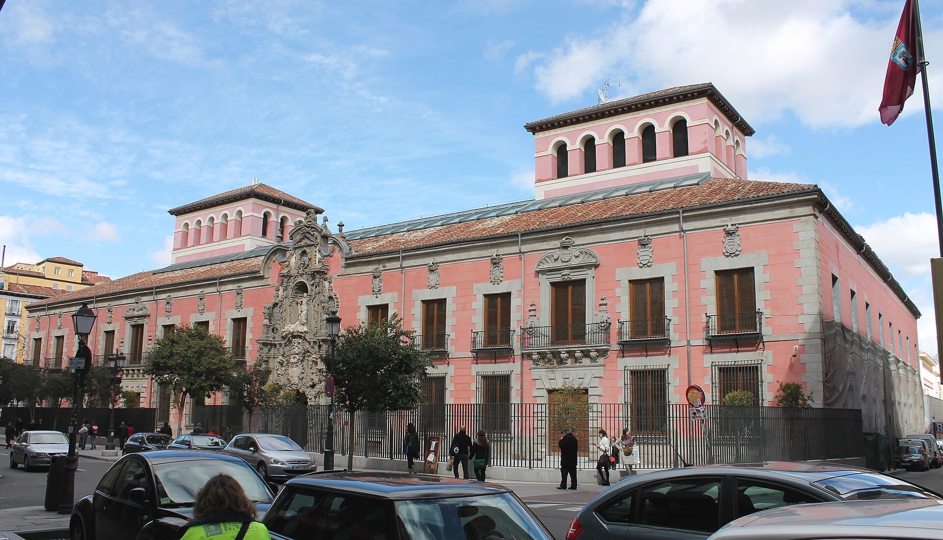 La facciata barocca rosa del Museo de Historia de Madrid con elaborate decorazioni in pietra, alte finestre e persone che passeggiano in una giornata di sole.