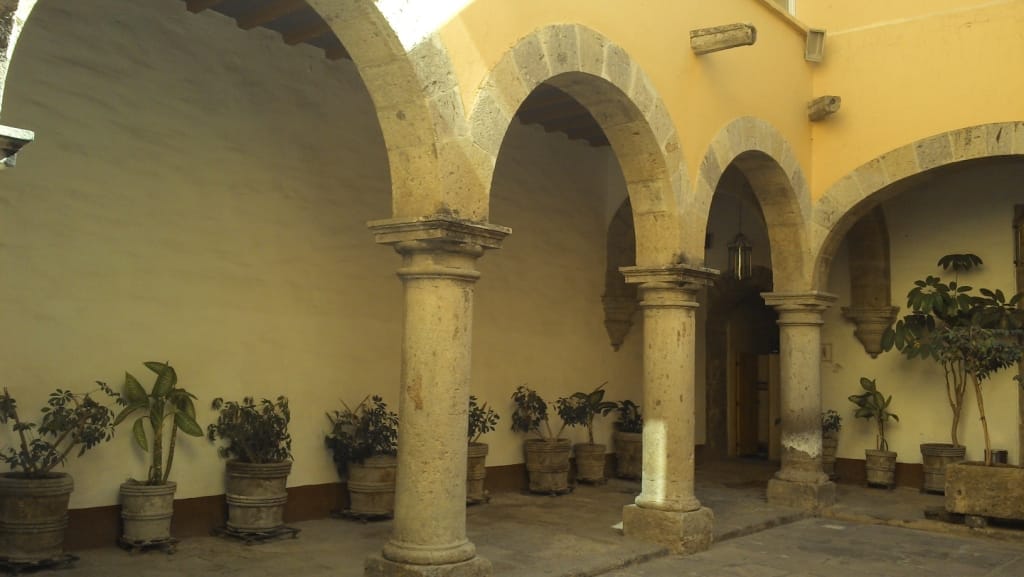 Archi in pietra e piante in vaso decorano il tranquillo cortile del Museo de la Ciudad de Guadalajara sotto la calda luce del pomeriggio.