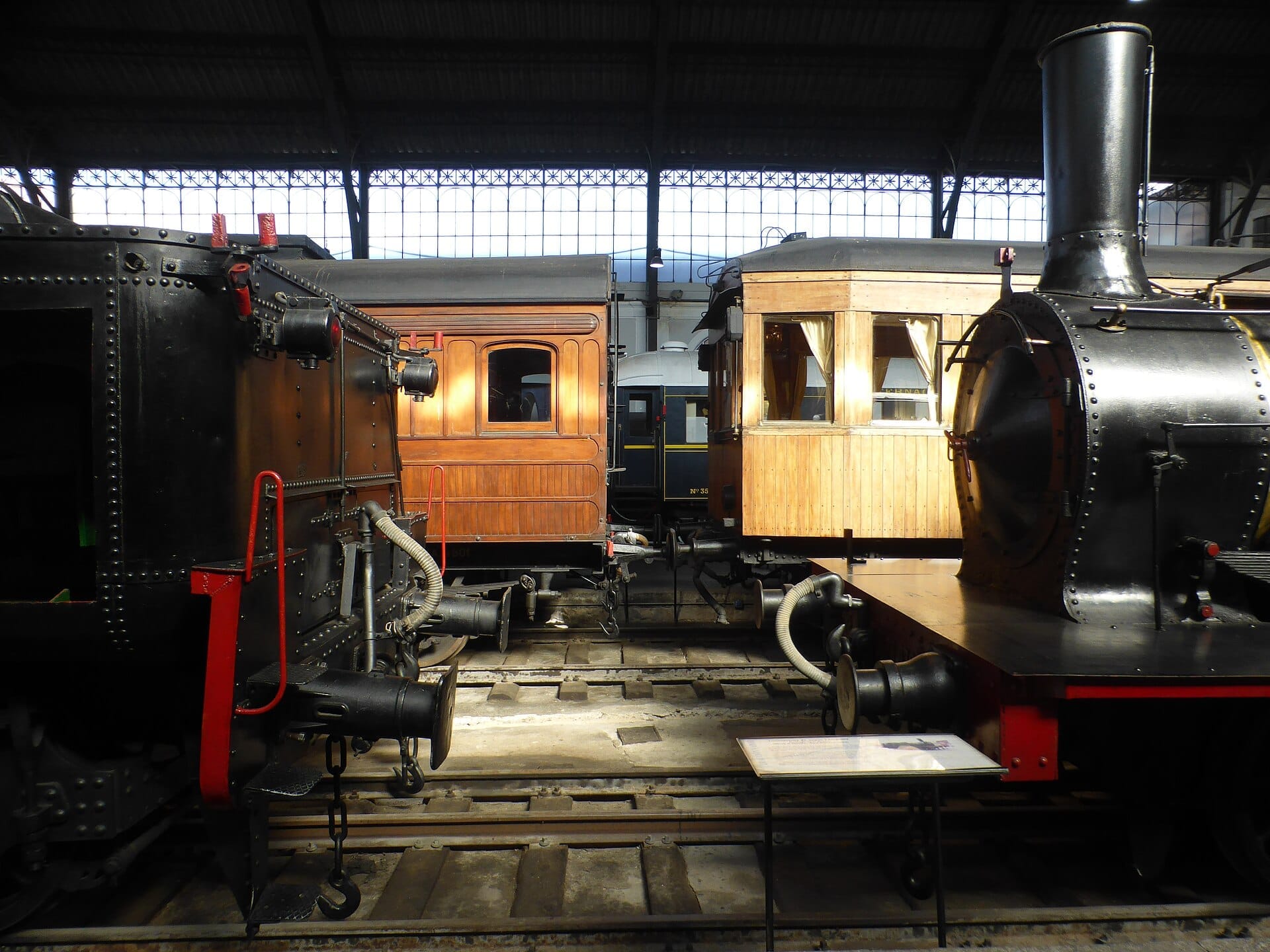 Locomotive a vapore vintage restaurate e carrozze passeggeri in legno all'interno della storica stazione ferroviaria Delicias del Museo del Ferrocarril de Madrid, illuminate dalla luce naturale.
