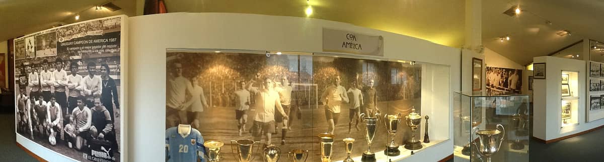 ภาพพาโนรามาภายใน Museo del Fútbol มอนเตวิเดโอ โชว์ภาพถ่ายประวัติศาสตร์ ถ้วยรางวัลและของสะสมฟุตบอลในแสงไฟอบอุ่น