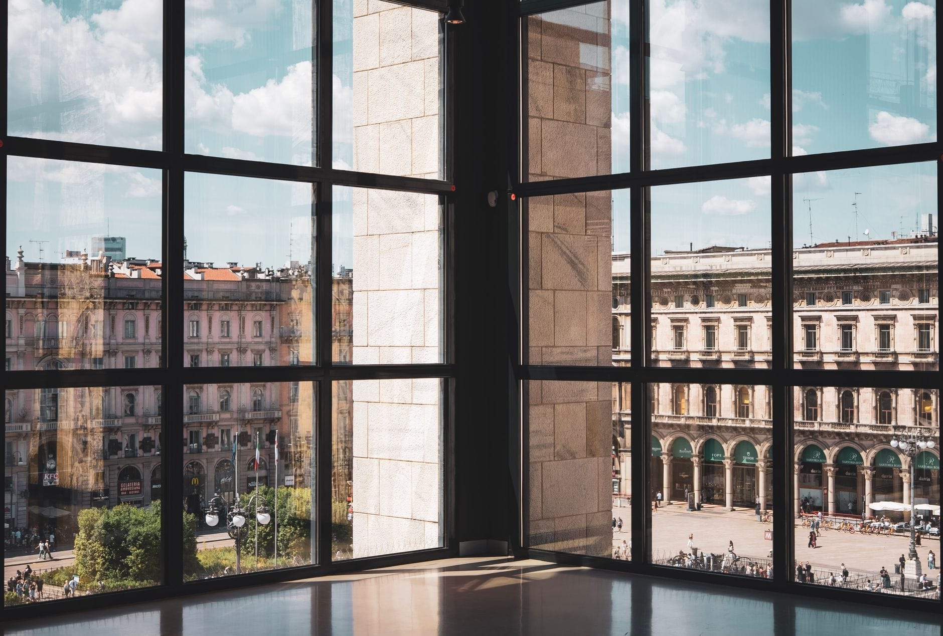 Vista della Piazza del Duomo e degli edifici storici attraverso grandi vetrate al Museo del Novecento a Milano, in una giornata di sole.