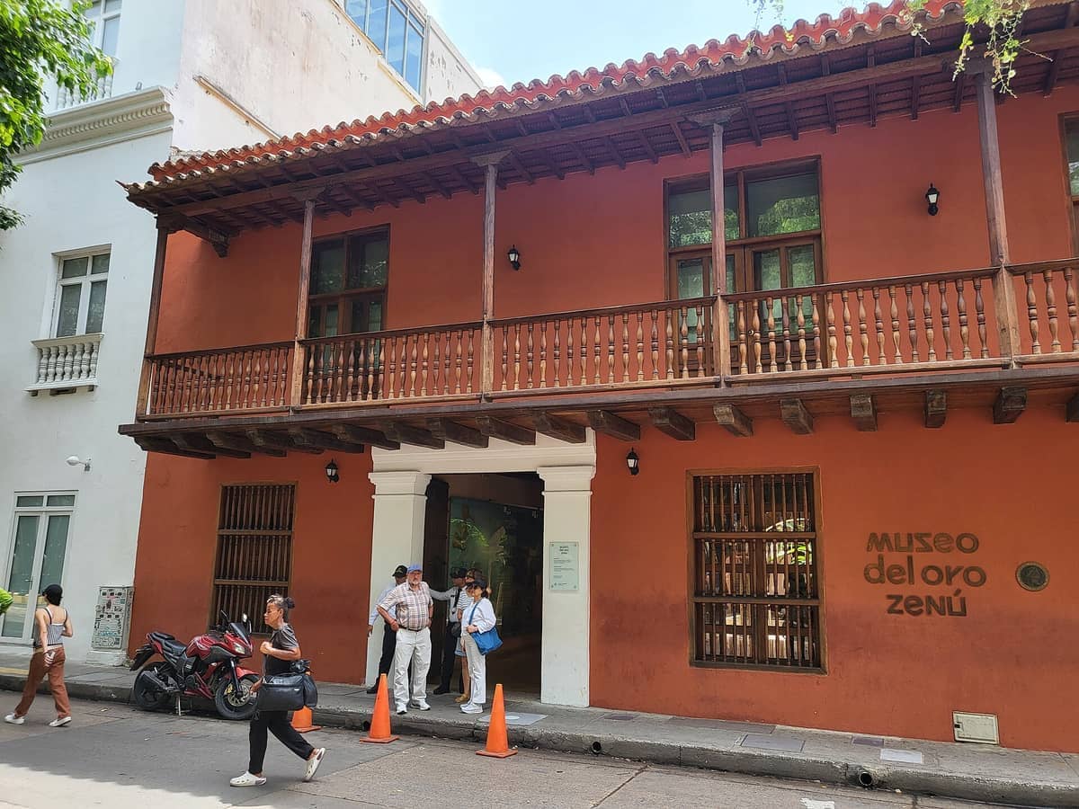Street view of Museo del Oro Zenú in Cartagena, featuring its terracotta façade, wooden balcony, and several visitors at the entrance.