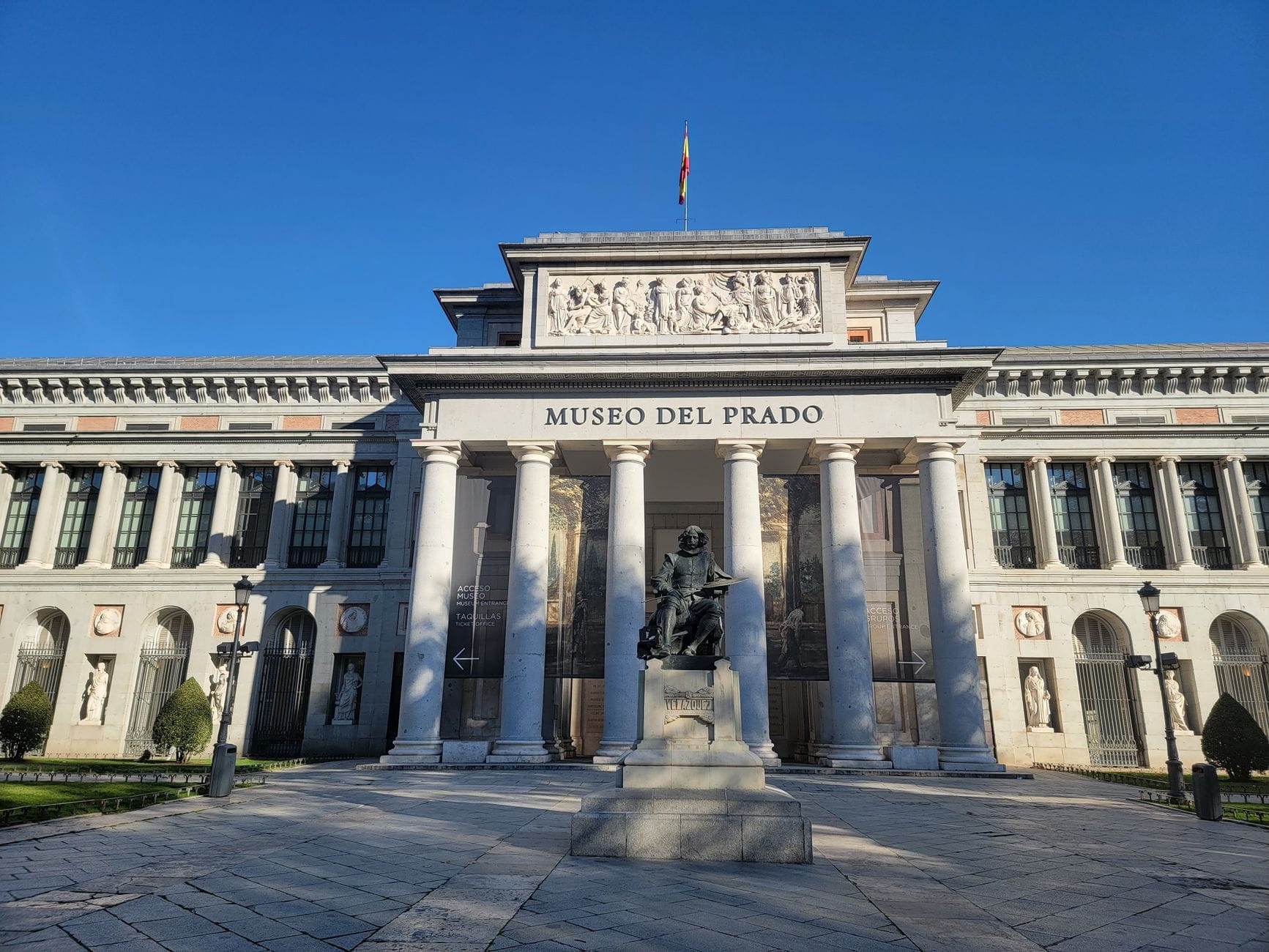 Facciata principale del Museo del Prado a Madrid con cielo azzurro, colonne classiche e statua, un invito a scoprire il più celebre museo d'arte della Spagna.