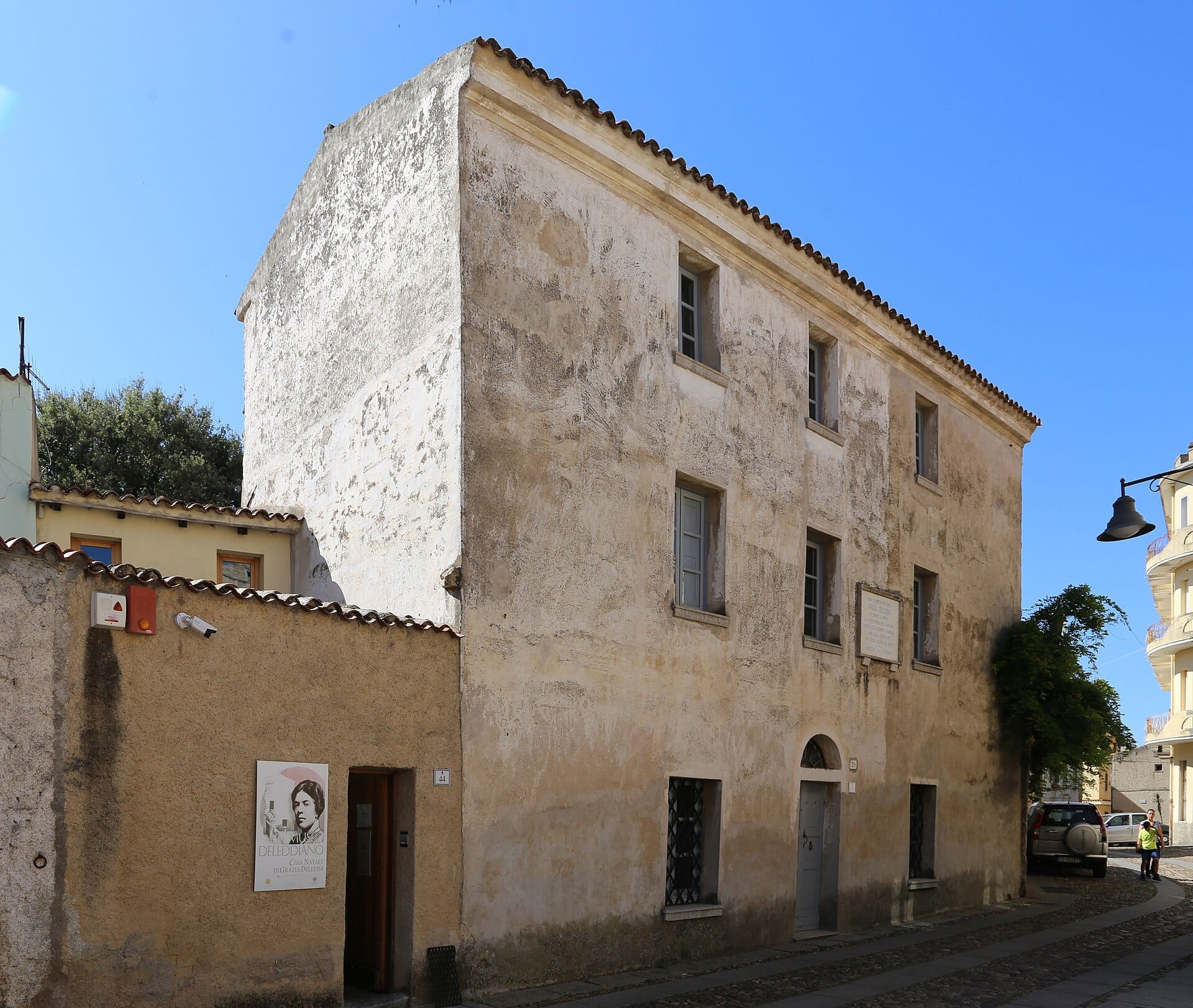 Die verwitterte Steinfassade des Museo Deleddiano mit grauen Fenstern unter einem klaren blauen Himmel im historischen Viertel von Nuoro.
