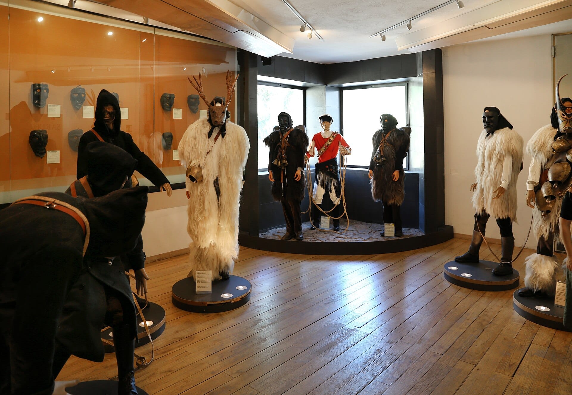 Ausstellungsraum im Museo delle Maschere Mediterranee mit traditionellen sardischen Karnevalskostümen und Masken auf Schaufensterpuppen, mit Holzböden und natürlichem Licht.