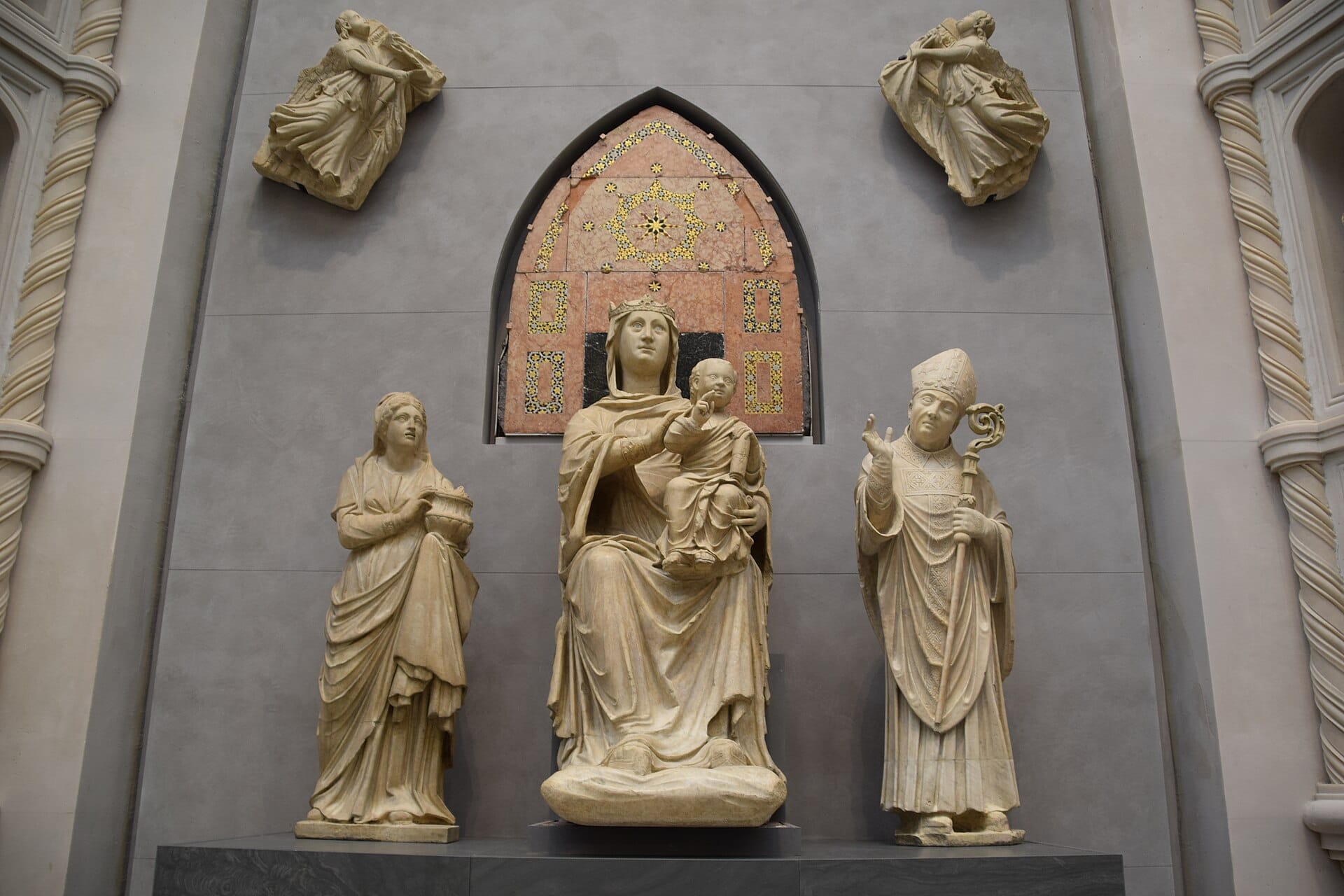 ประติมากรรมและกลุ่มรูปแกะสลักจัดแสดงภายใน Museo dell'Opera del Duomo เมืองฟลอเรนซ์ มีรูปพระเป็นหลักและผนังสีเทาตกแต่งอยู่ด้านหลัง