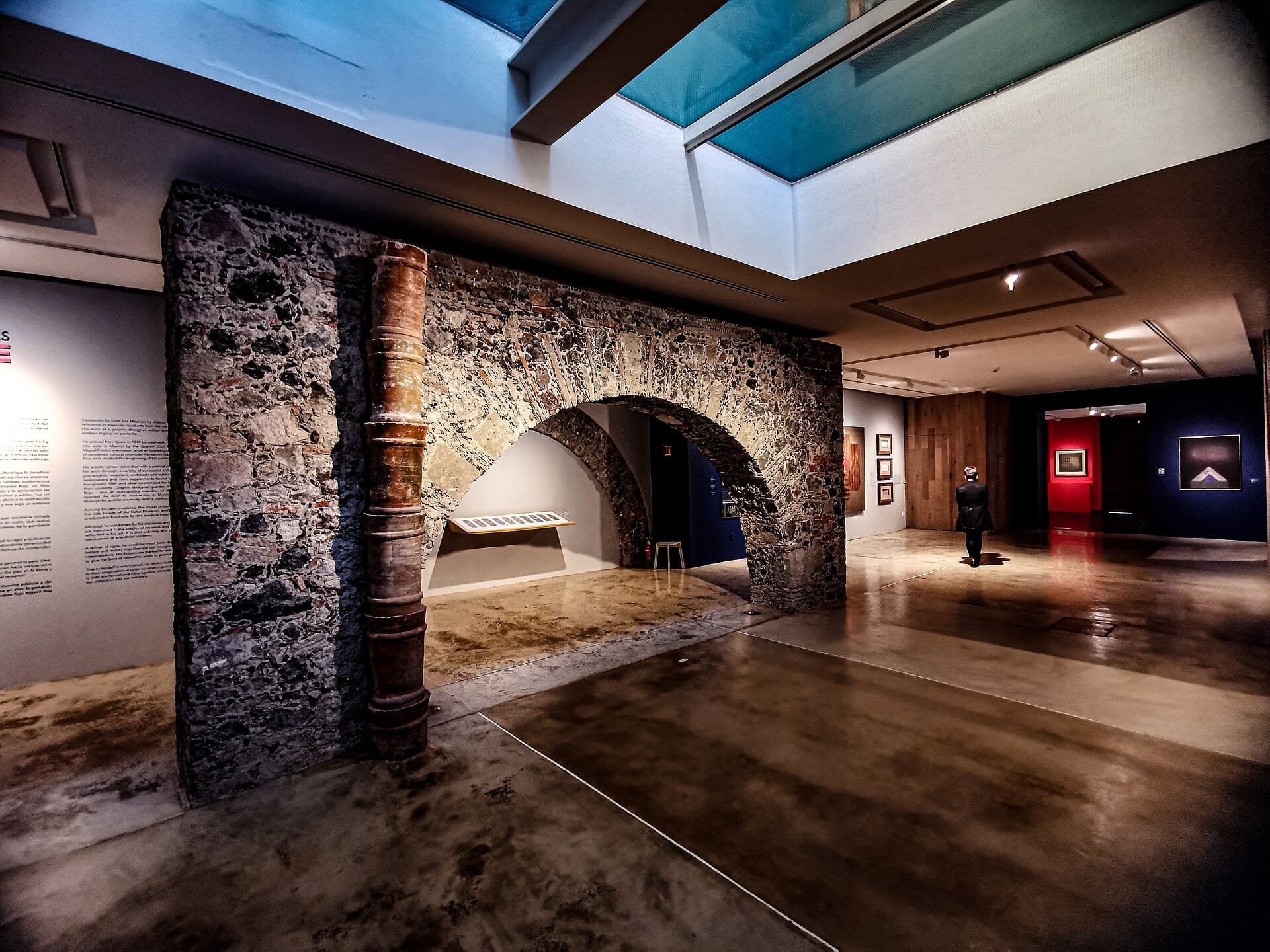Archi in pietra e lucernari moderni all'interno del Museo Kaluz, con esposizioni d'arte e dettagli architettonici coloniali in una calda illuminazione ambientale.