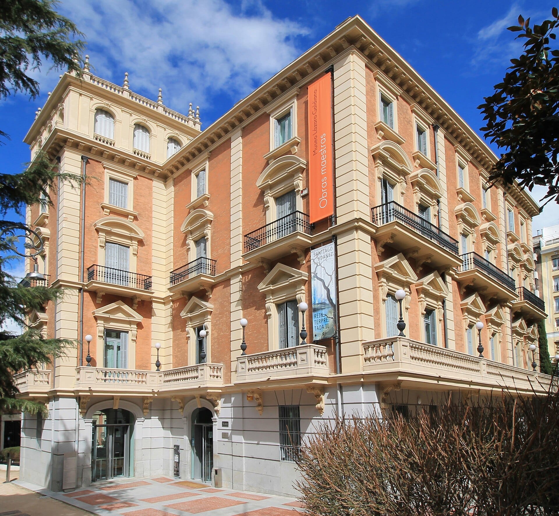 Vista esterna del Museo Lázaro Galdiano, un grande palazzo dei primi del Novecento con finestre ornate e striscioni sotto un cielo azzurro e soleggiato.