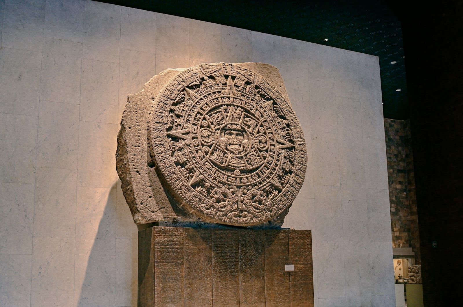 La Pietra del Sole azteca esposta al Museo Nacional de Antropología, davanti a una parete di pietra neutra dolcemente illuminata all'interno del museo.