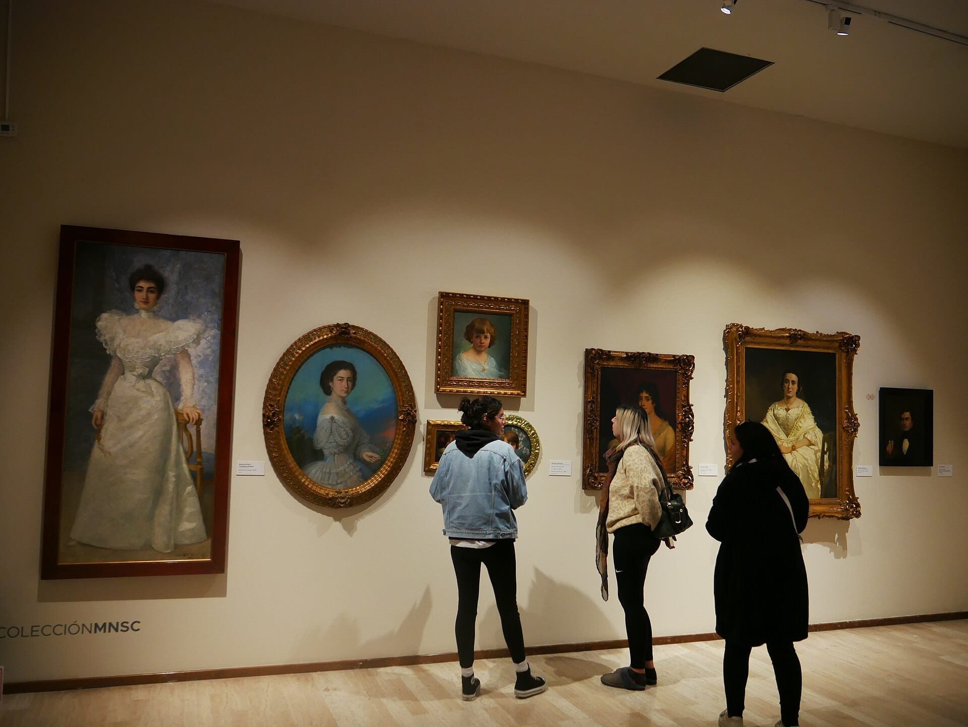 Visitatori che osservano una collezione di dipinti classici di ritratti europei al Museo Nacional de San Carlos, esposti in elaborati cornici dorate su una parete di galleria ben illuminata.