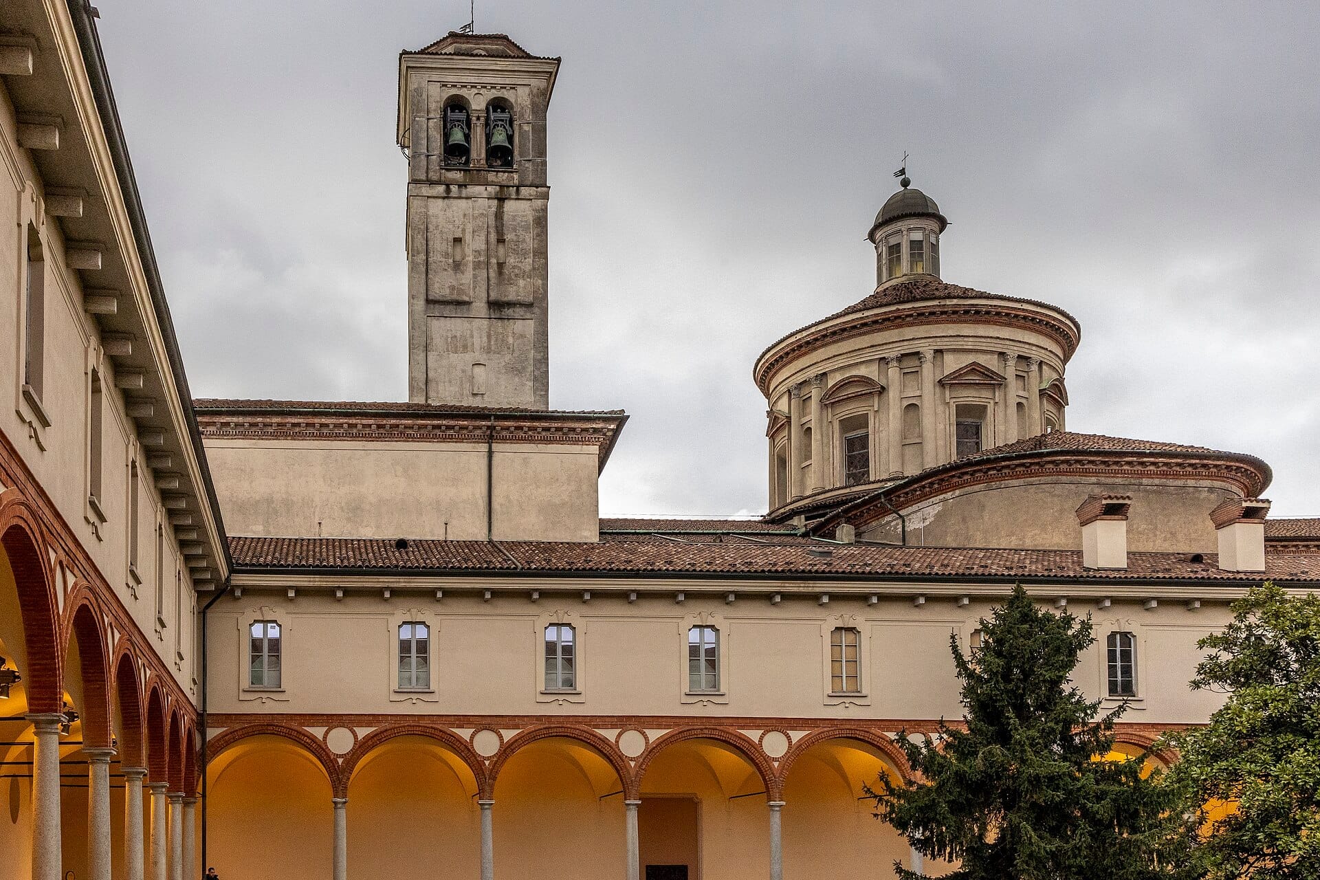 Vista esterna del Museo Nazionale della Scienza e della Tecnologia Leonardo da Vinci, con gli archi del chiostro e l'architettura storica del monastero sotto un cielo nuvoloso.