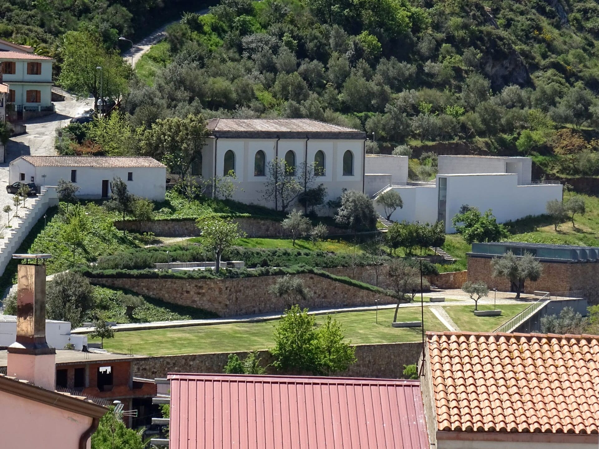 Außenansicht des Museo Nivola in Orani, Sardinien, umgeben von Terrassengärten, weißen Gebäuden und üppigen grünen Hügeln.