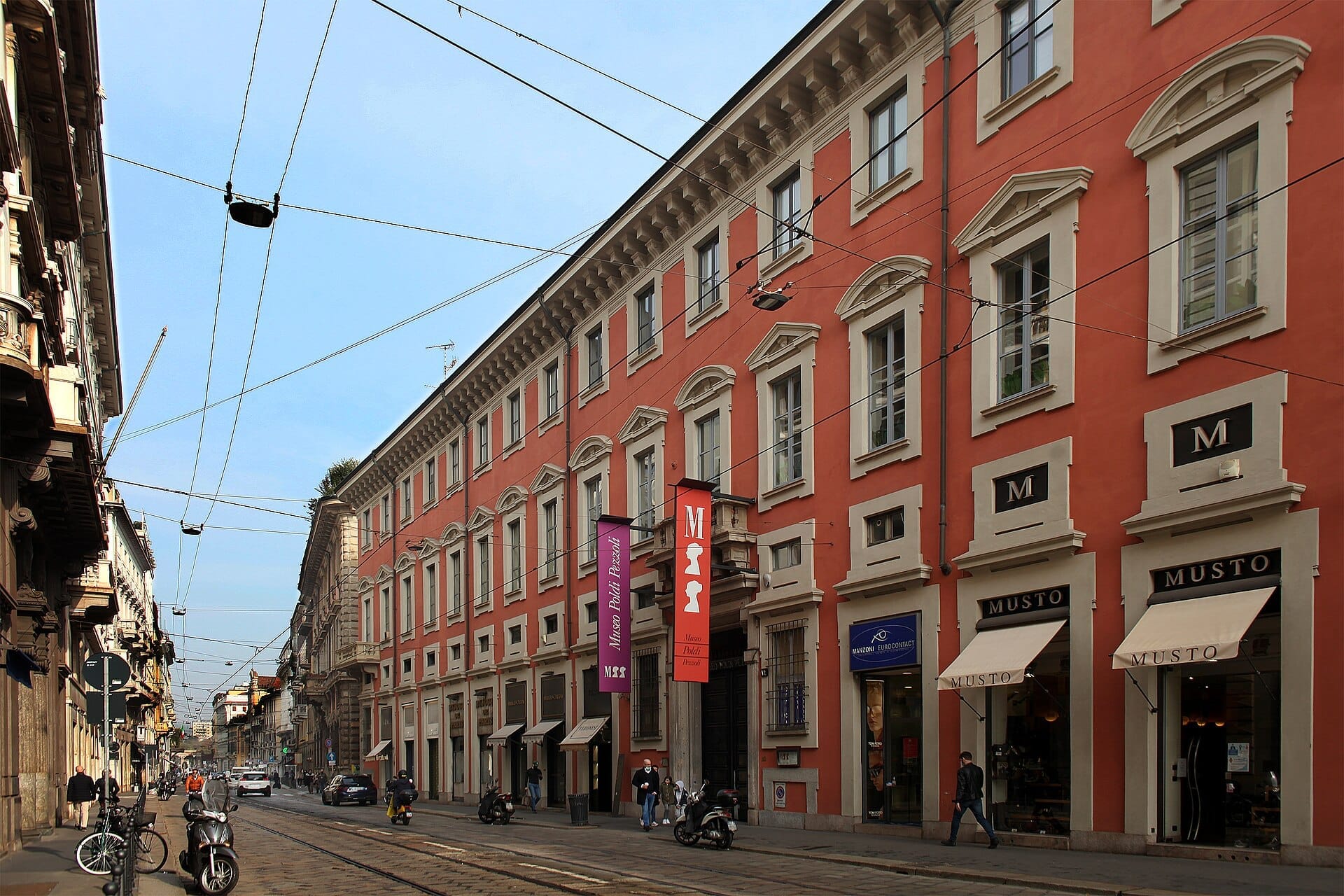 L'esterno del Museo Poldi Pezzoli a Milano, con un grande edificio color corallo lungo Via Manzoni con persone che passeggiano.