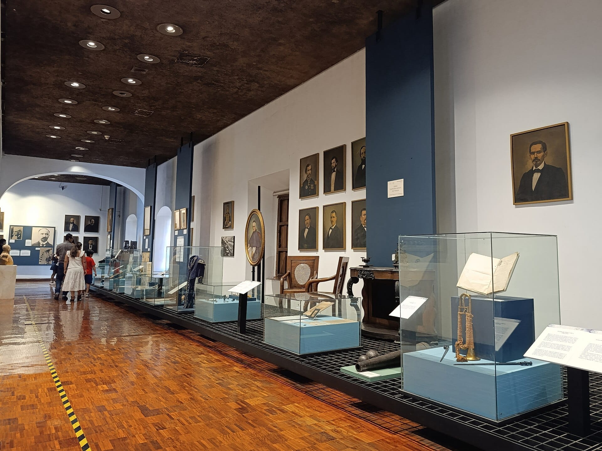 Sala espositiva all'interno del Museo Regional de Guadalajara con teche in vetro, reperti storici, pavimenti in legno e ritratti lungo le pareti bianche e blu.