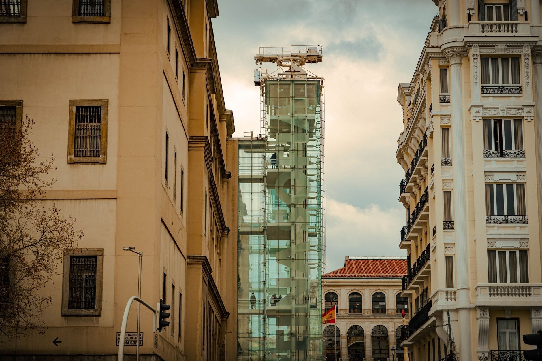Vista esterna del Museo Reina Sofía a Madrid, con le iconiche torri ascensore in vetro e gli storici edifici circostanti sotto un cielo nuvoloso e suggestivo.