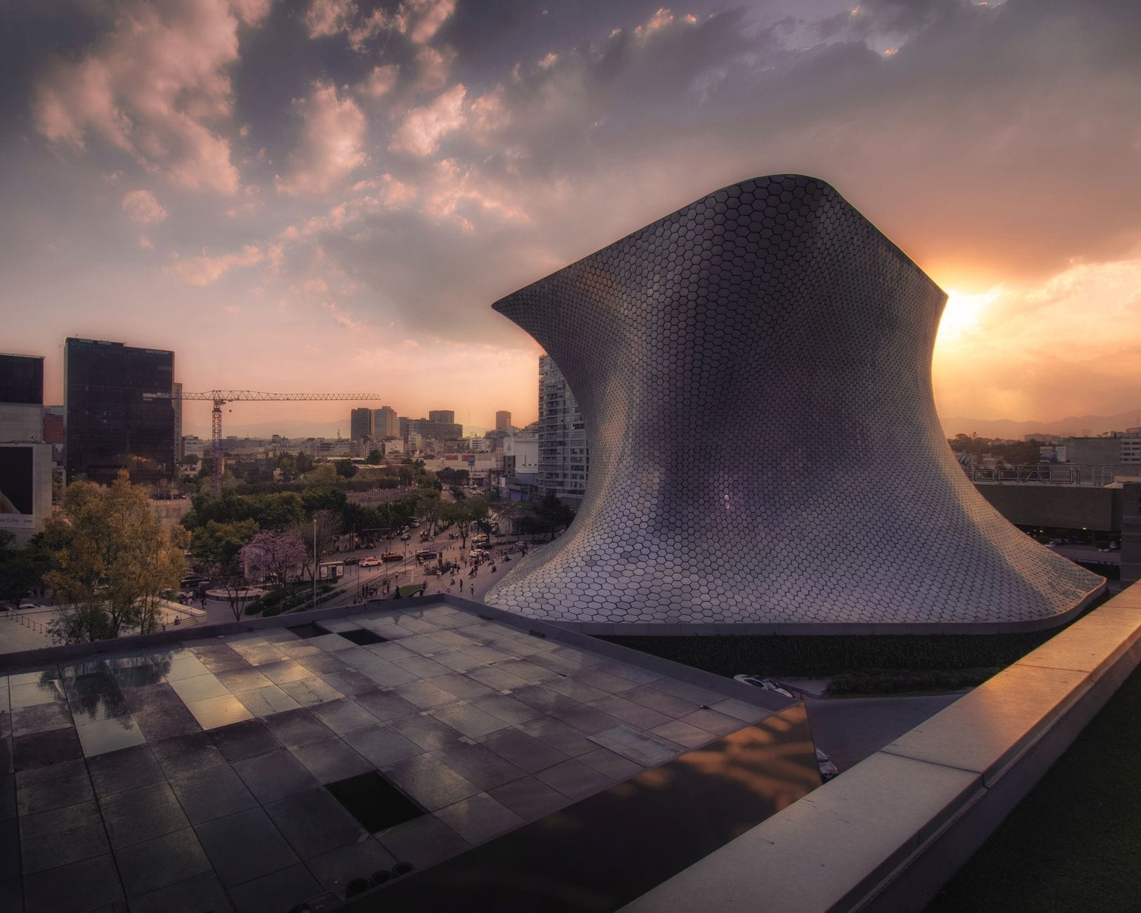 Vista panoramica al tramonto della celebre facciata curva e argentea del Museo Soumaya, con cielo drammatico e skyline sullo sfondo: un invito a scoprire questo museo d'arte gratuito a Città del Messico.