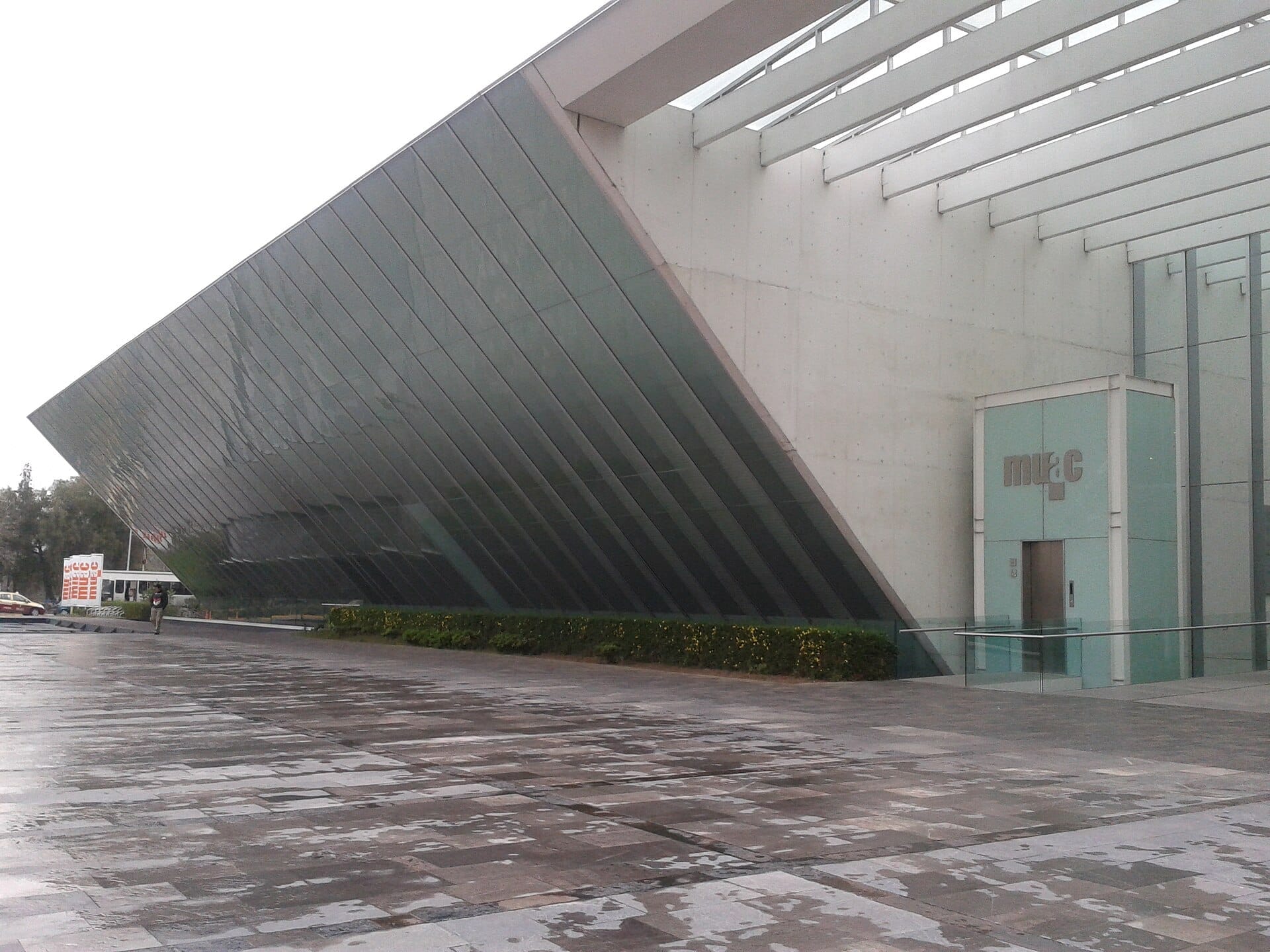 Facciata angolare in cemento e vetro del Museo Universitario Arte Contemporáneo (MUAC), con linee architettoniche moderne e un'ampia piazza in pietra antistante.