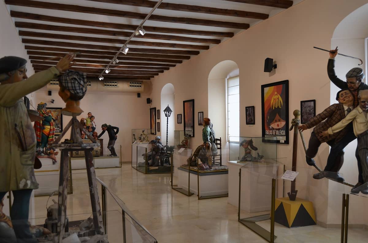 Raum im Museu Faller de València mit bunten Ninots, satirischen Skulpturen des Las Fallas-Festivals, unter Holzdeckenbalken und natürlichem Fensterlicht.