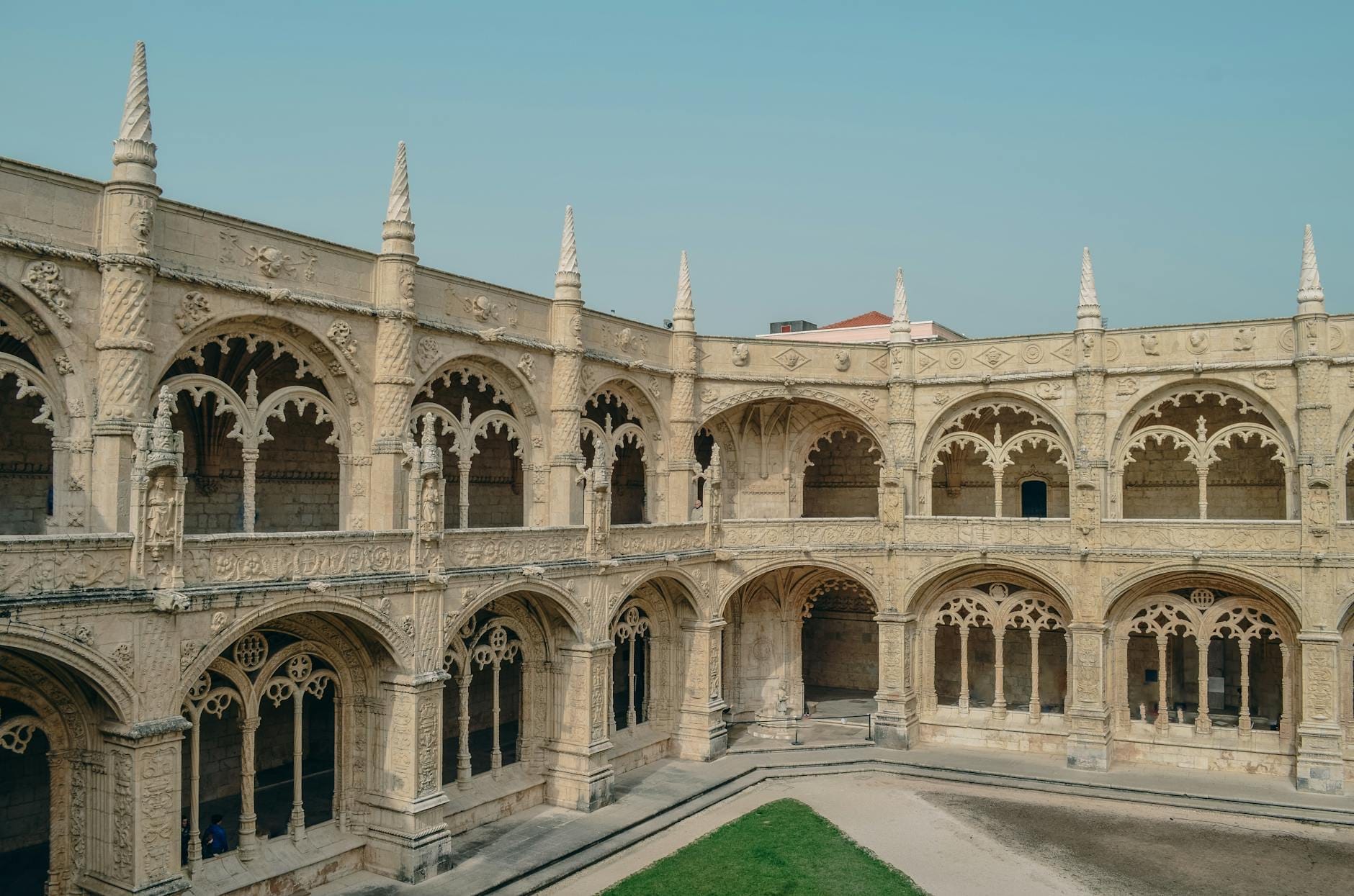 Vista mozzafiato dei chiostri in pietra ornata del Monastero dos Jerónimos, con archi e guglie sotto un cielo limpido, a testimonianza dell'architettura storica portoghese.