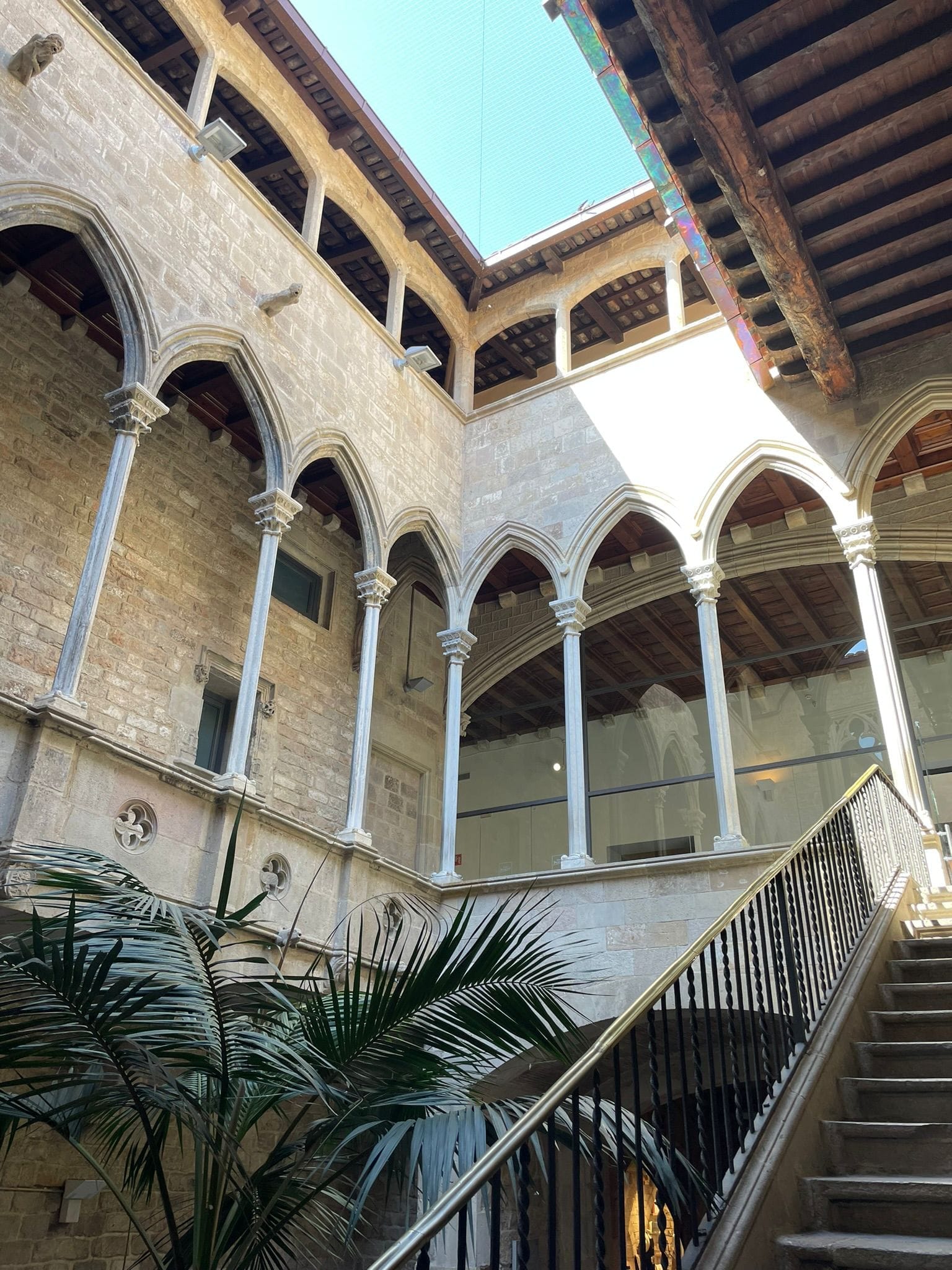 Stone courtyard of Museu Picasso Barcelona with arched windows, palm plants, and a staircase under natural daylight.