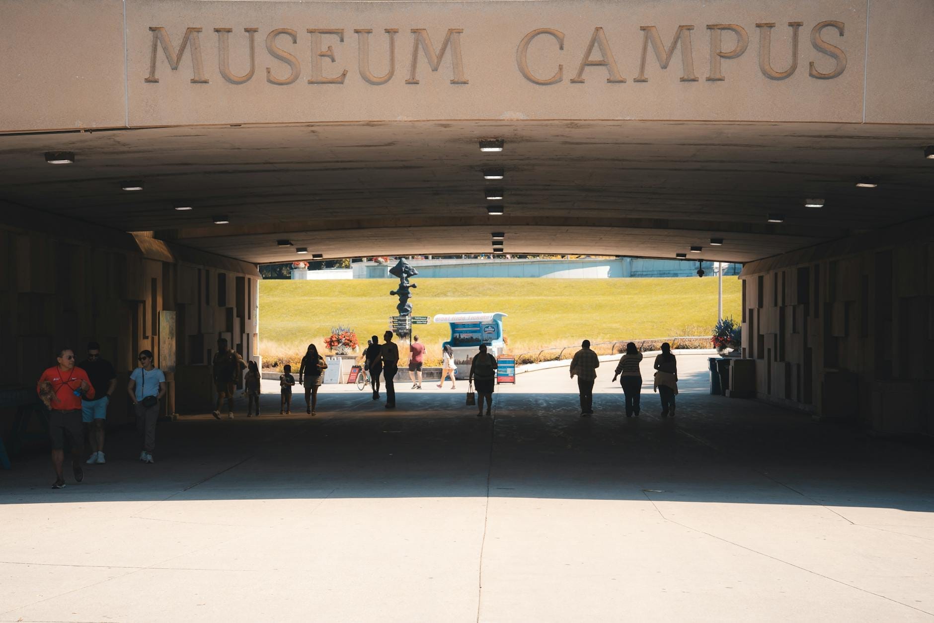 ผู้คนเดินผ่านทางเข้าอุโมงค์ ‘Museum Campus’ สู่พื้นที่กลางแจ้ง มีบรรยากาศสดใส เป็นตัวแทน Museum Campus ในชิคาโกที่ชวนให้น่าเที่ยว