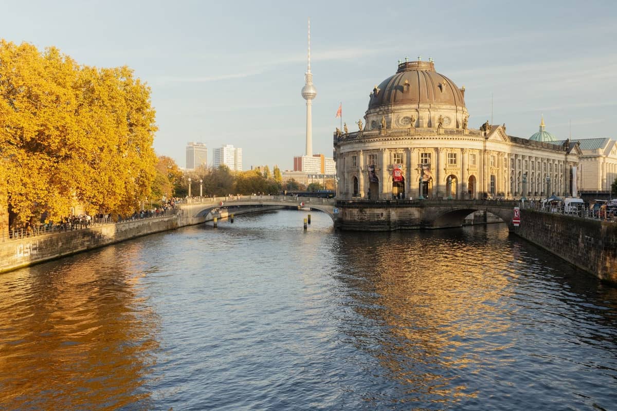 La Isla de los Museos en Berlín con el Bode-Museum, la torre de televisión al fondo y el río Spree en primer plano en un día soleado.