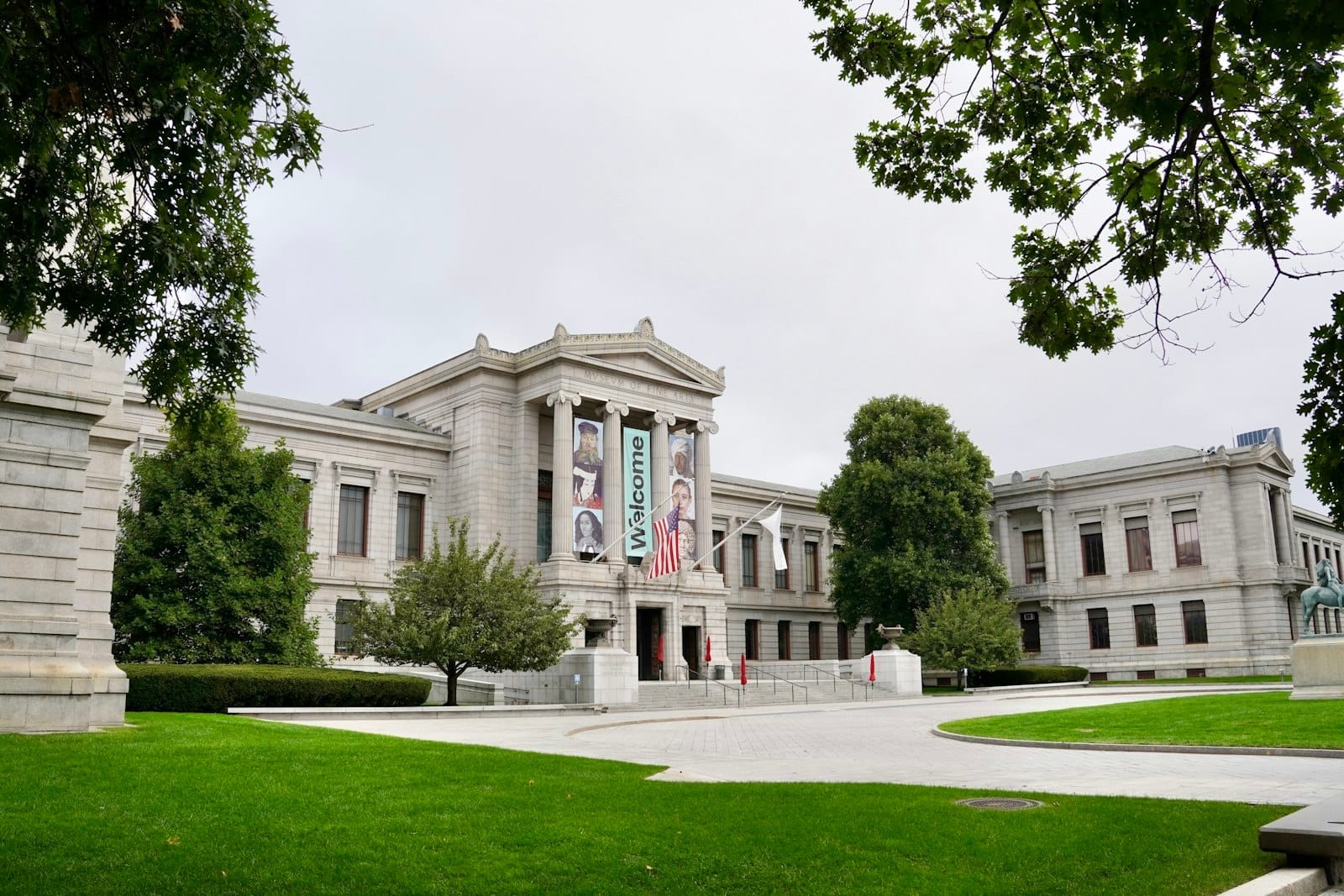 Il Museum of Fine Arts di Boston, con la sua grandiosa facciata in pietra, la bandiera americana e i banner di benvenuto, incorniciato da lussureggianti prati e alberi.