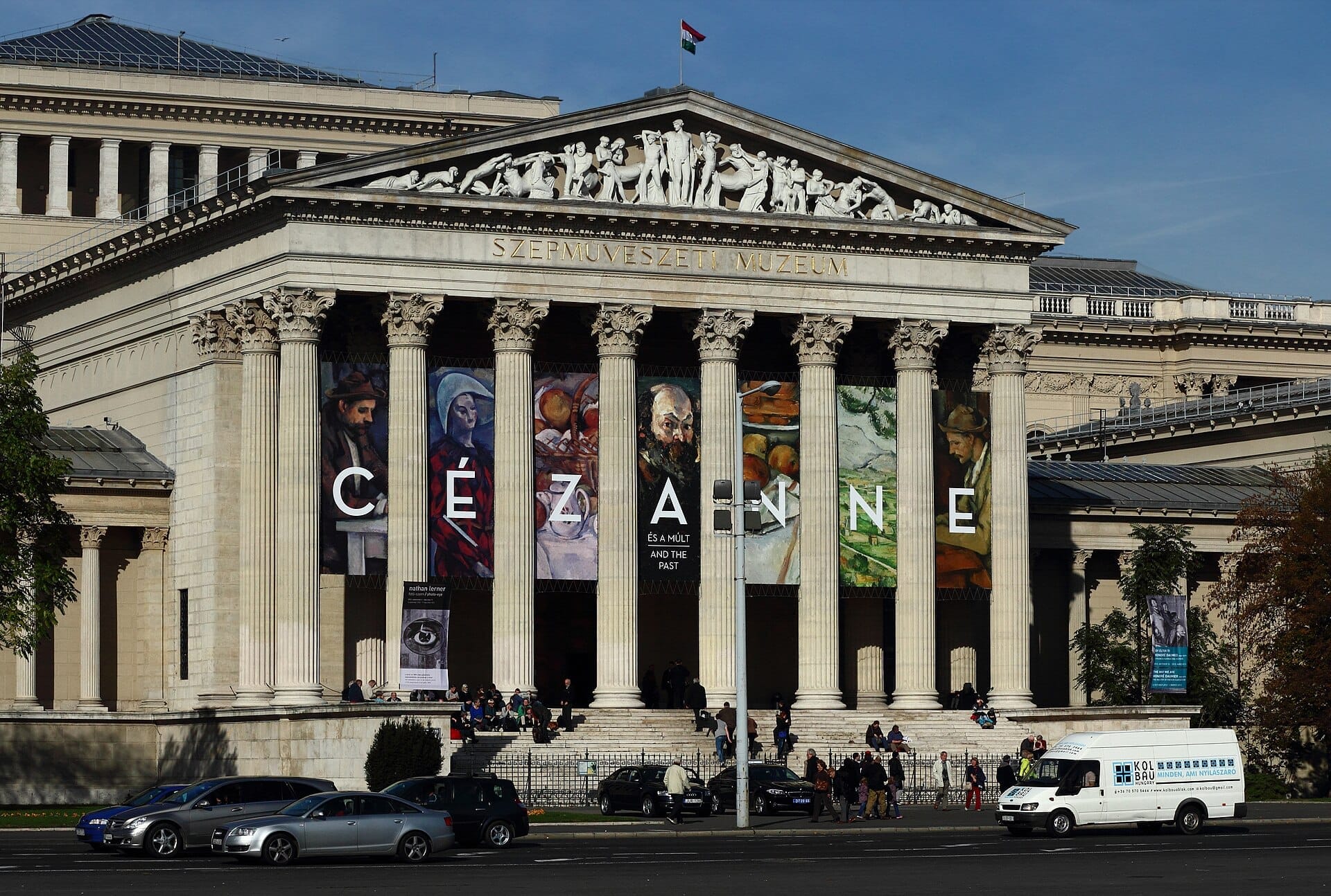 Ang neoclassical na fasad ng Museum of Fine Arts Budapest na may malalaking haligi, mga banner na nagtatampok ng mga obra ni Cézanne, at mga bisita na nagtitipon sa pasukan.